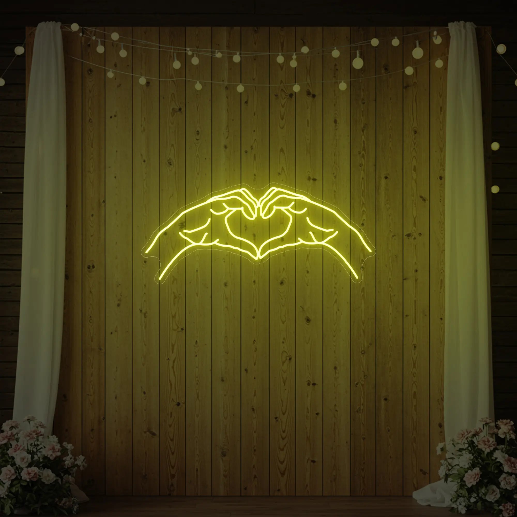 Photo of the 'Heart Hands' neon sign glowing in lemon yellow against a styled interior wall.