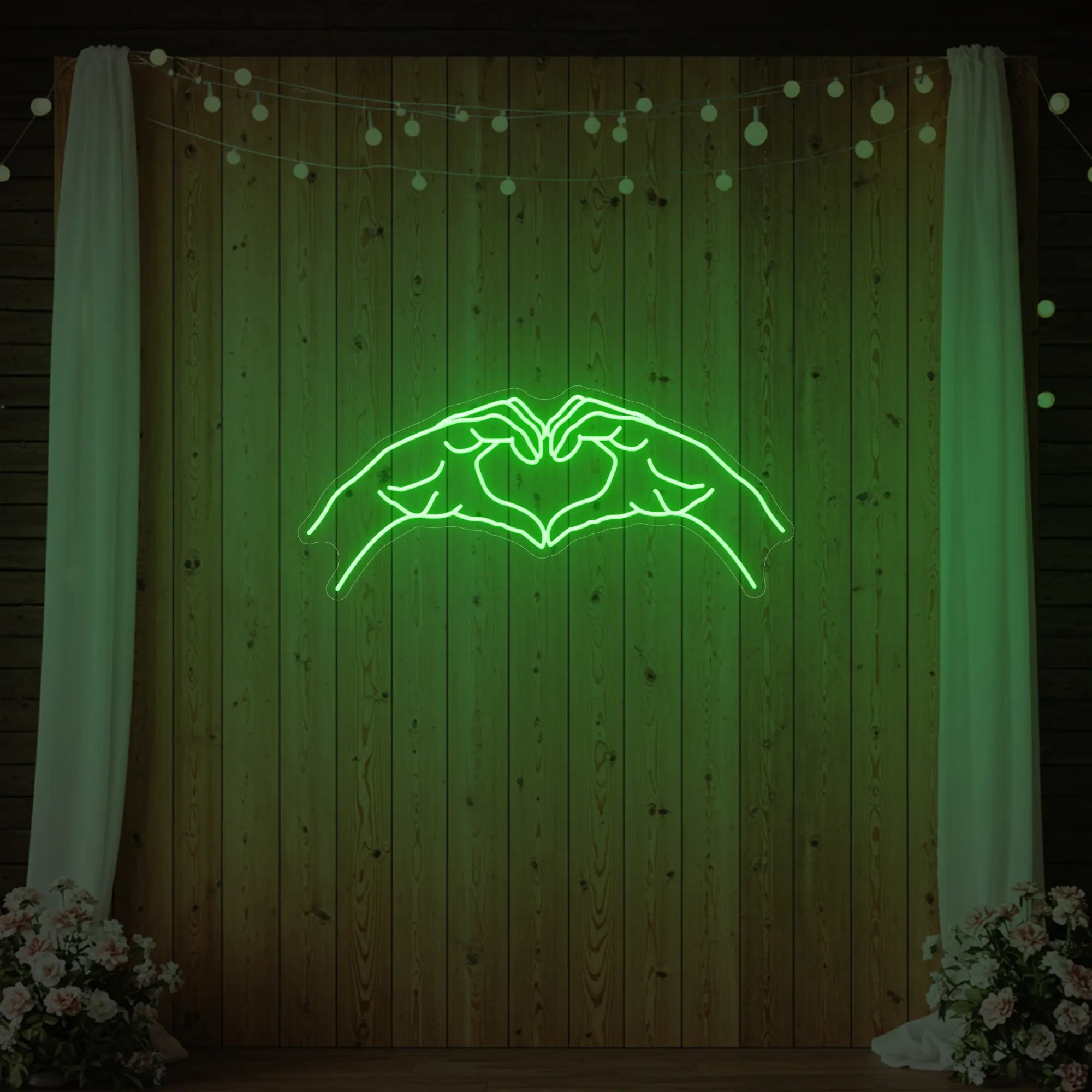 Photo of the 'Heart Hands' neon sign glowing in green against a styled interior wall.