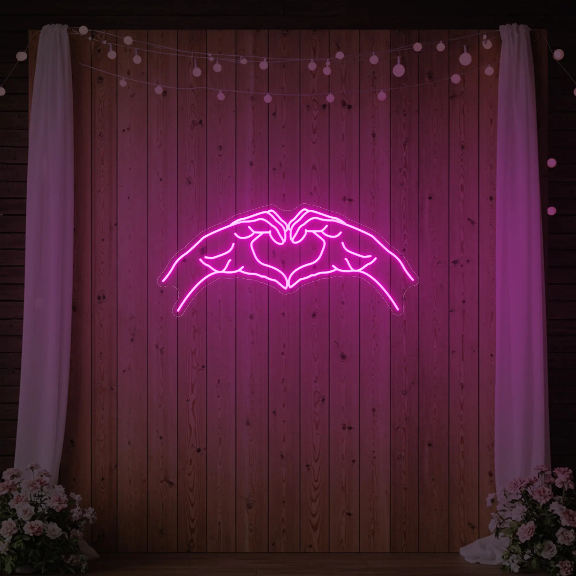 Photo of the 'Heart Hands' neon sign glowing in light pink against a styled interior wall.