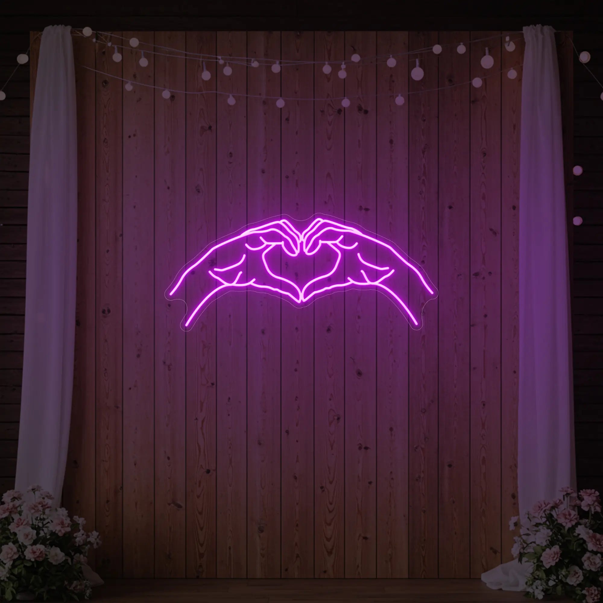 Photo of the 'Heart Hands' neon sign glowing in deep pink against a styled interior wall.