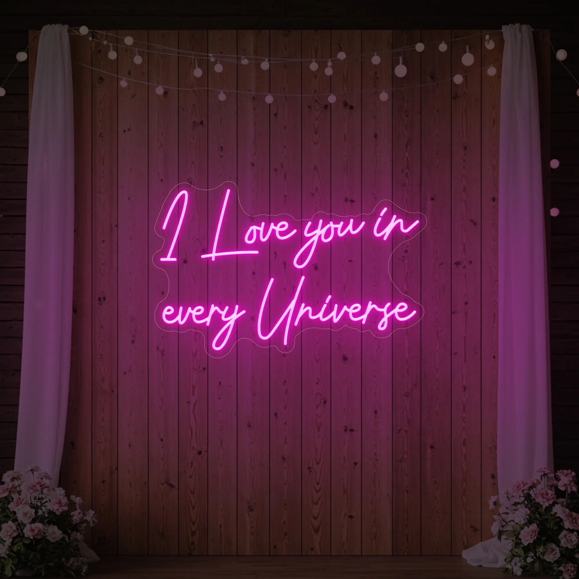 Photo of the 'I Love You In Every Universe' neon sign glowing in light pink against a styled interior wall.