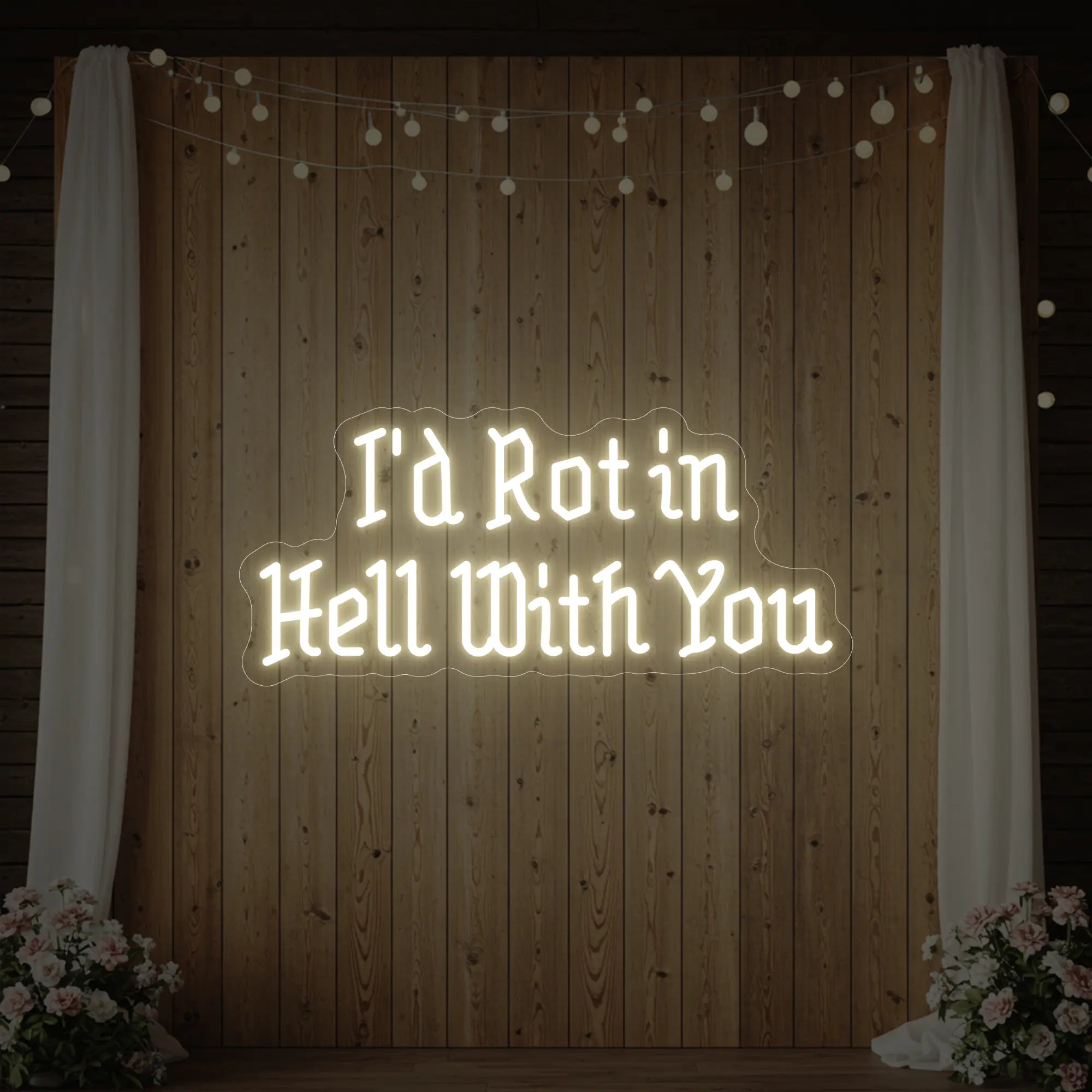 Photo of the 'I’d Rot in Hell With You' neon sign glowing in warm white against a styled interior wall.