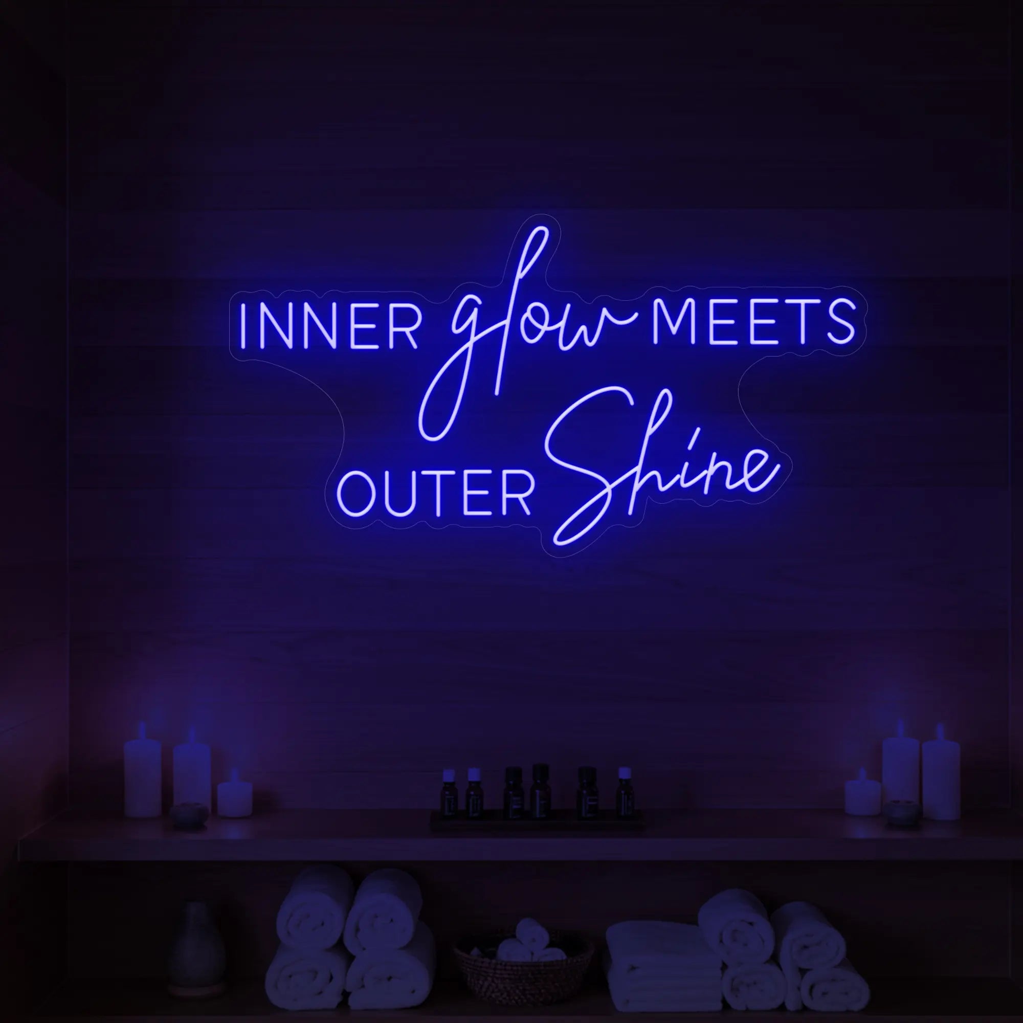 Photo of the 'INNER glow MEETS OUTER Shine' neon sign glowing in deep blue against a styled interior wall.