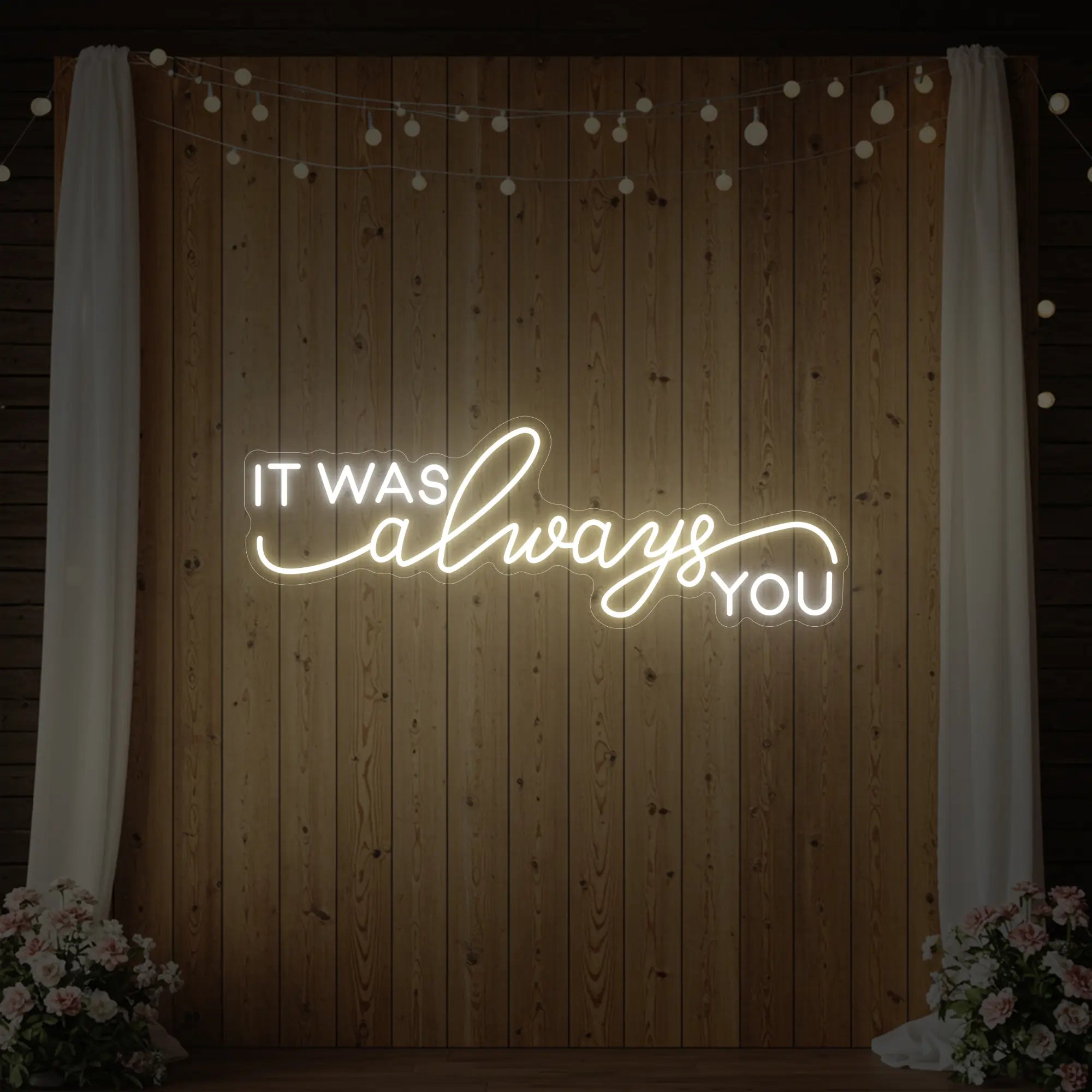 Photo of the 'It Was Always You' neon sign glowing in warm white against a styled interior wall.