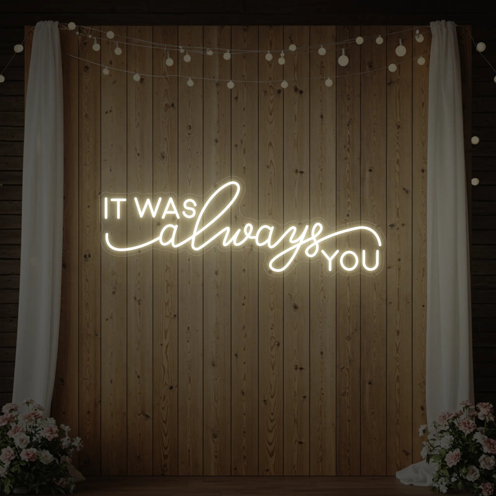 Photo of the 'It Was Always You' neon sign glowing in warm white against a styled interior wall.