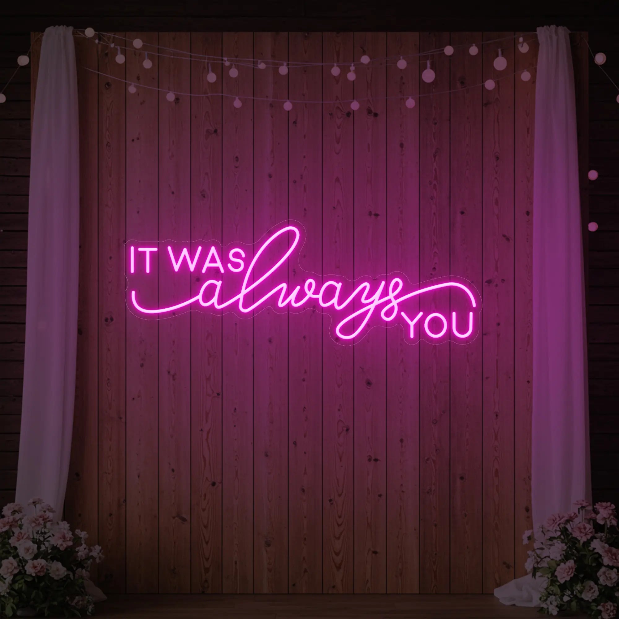 Photo of the 'It Was Always You' neon sign glowing in light pink against a styled interior wall.