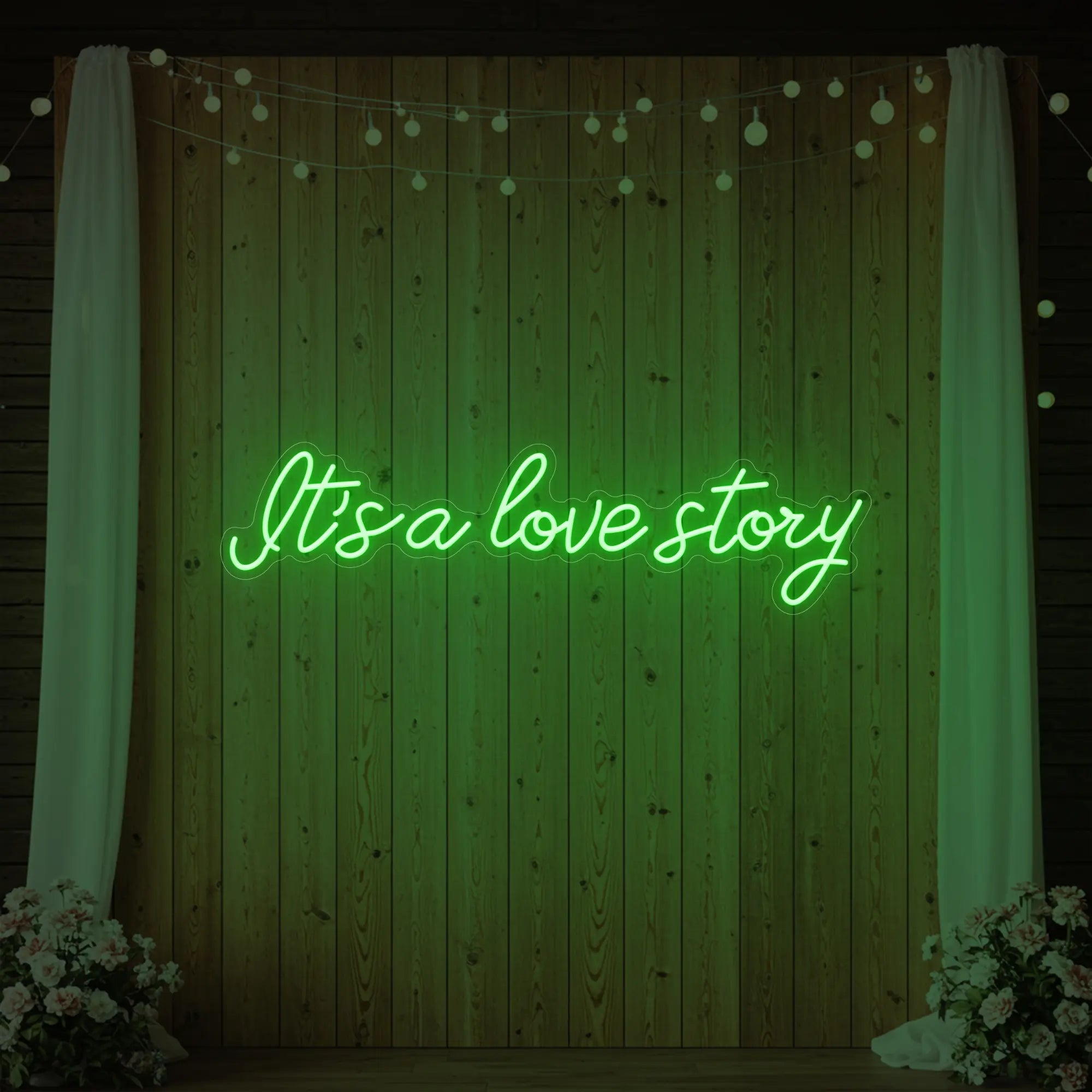 Photo of the 'It’s a Love Story' neon sign glowing in green against a styled interior wall.