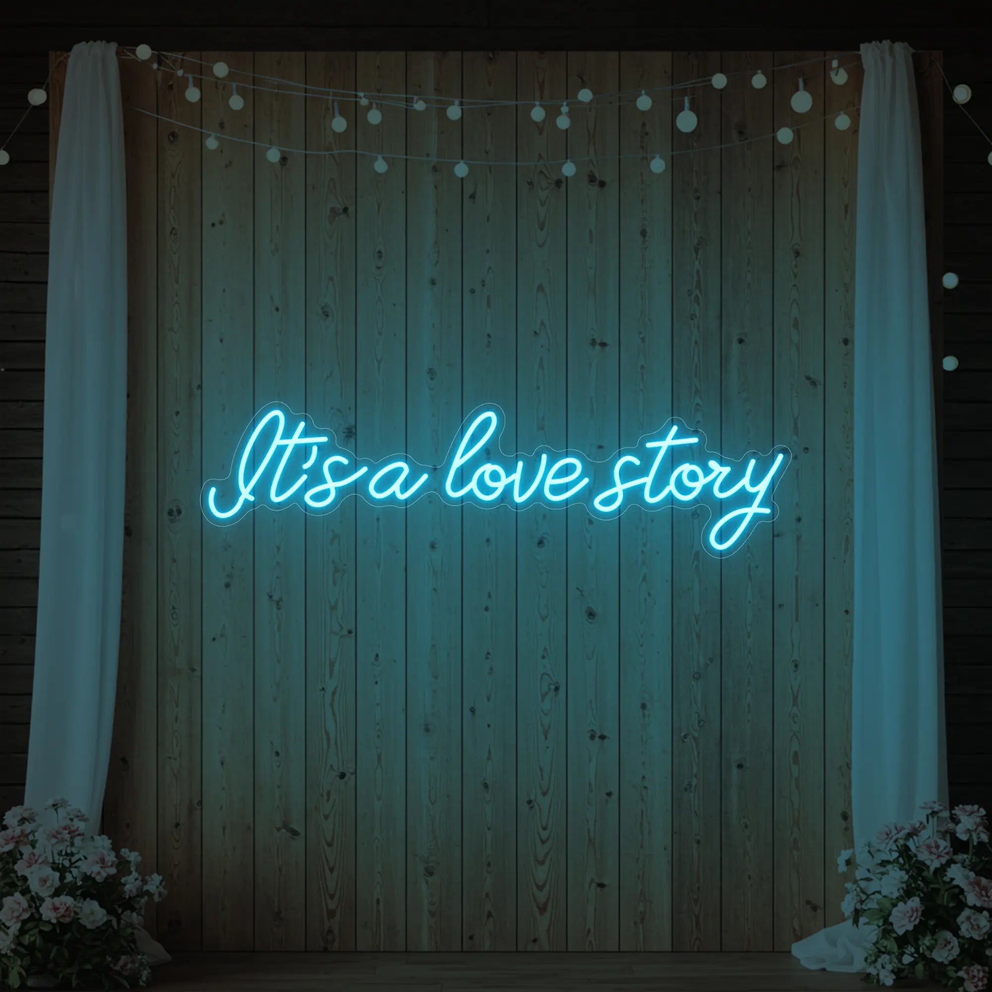 Photo of the 'It’s a Love Story' neon sign glowing in ice blue against a styled interior wall.