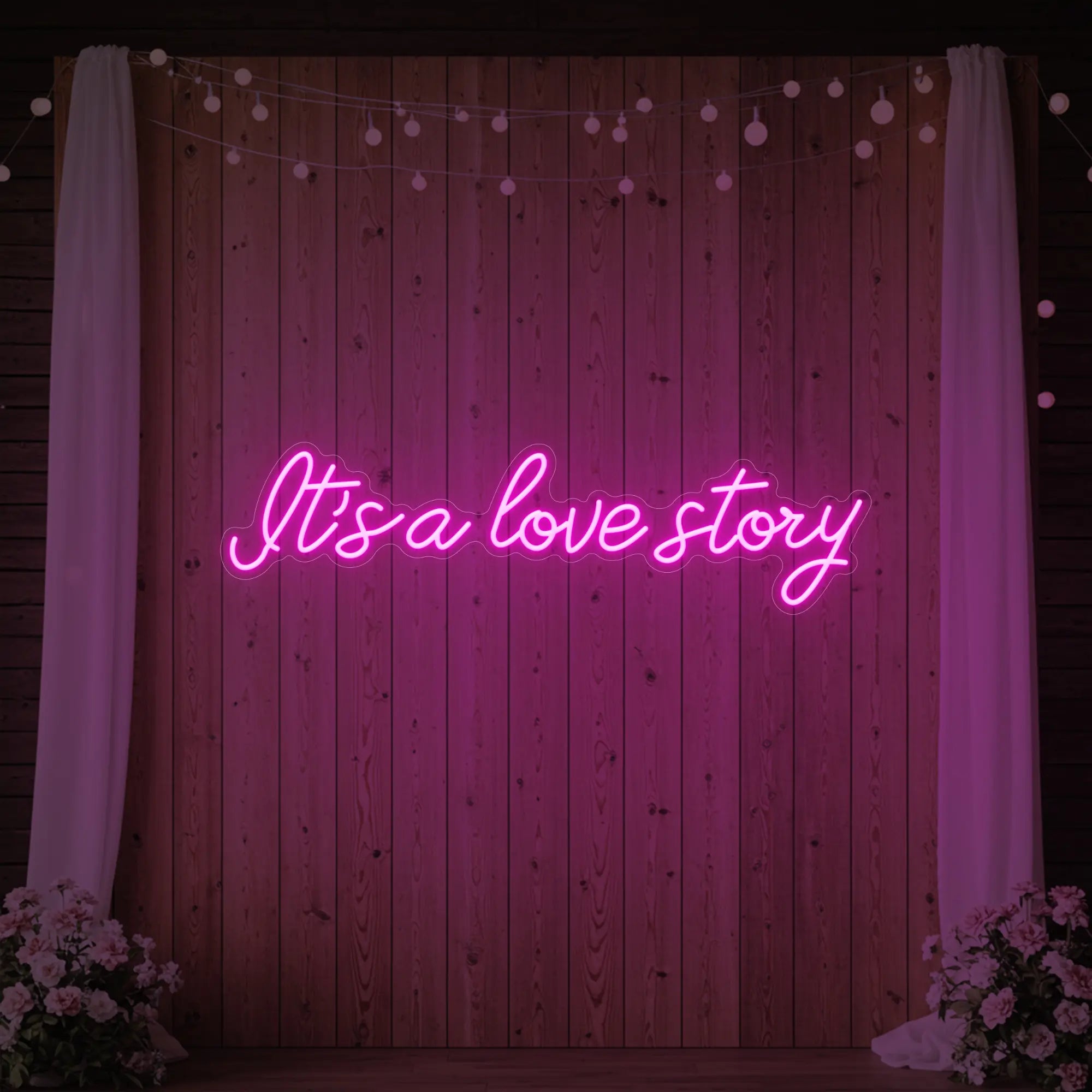 Photo of the 'It’s a Love Story' neon sign glowing in light pink against a styled interior wall.
