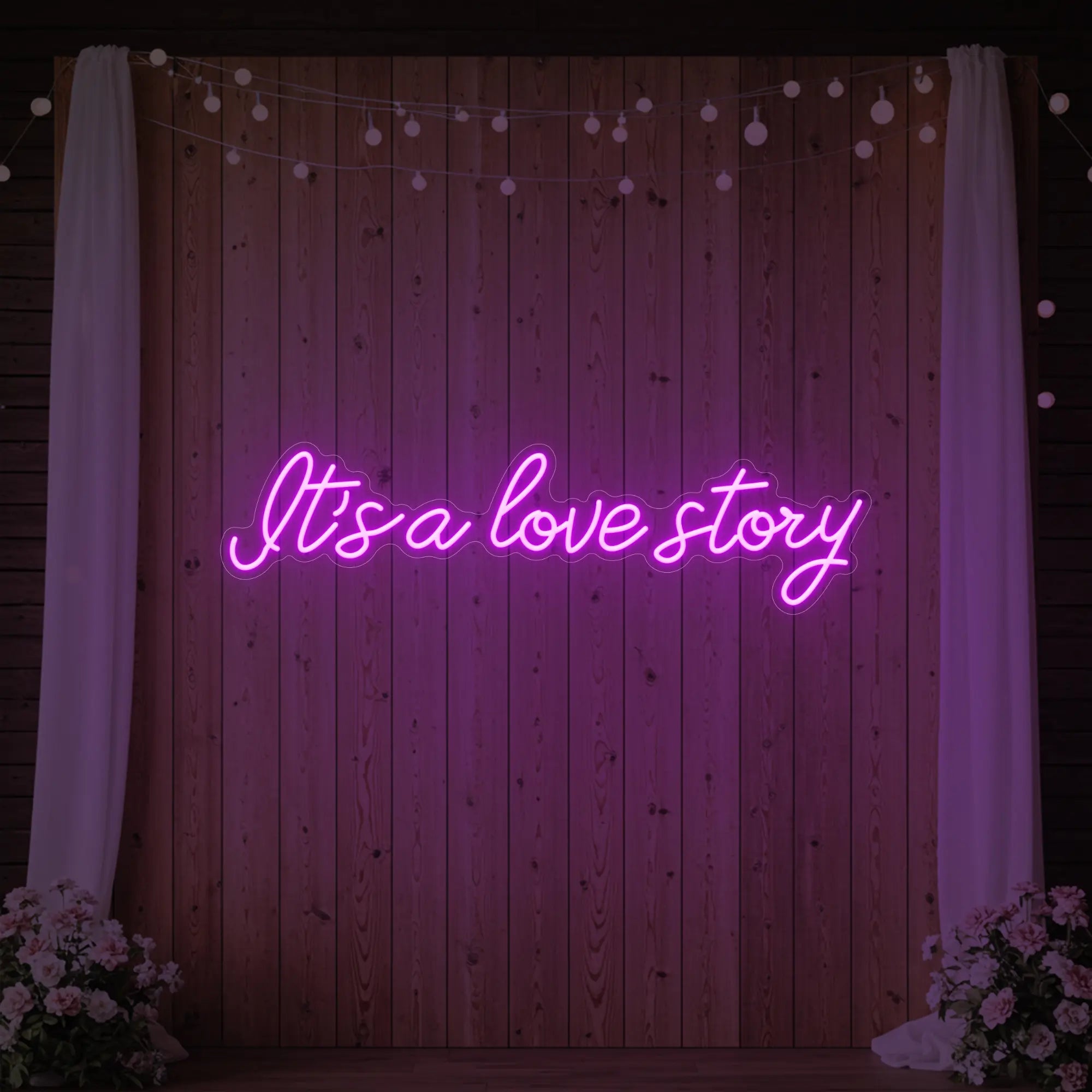 Photo of the 'It’s a Love Story' neon sign glowing in deep pink against a styled interior wall.