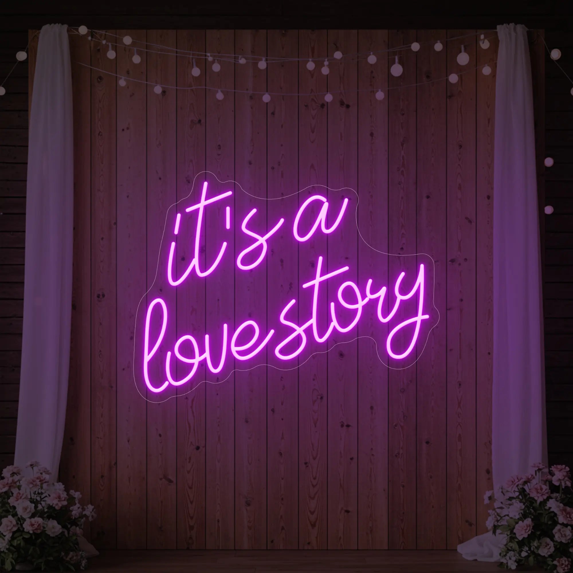 Photo of the 'It’s a Love Story' neon sign glowing in deep pink against a styled interior wall.