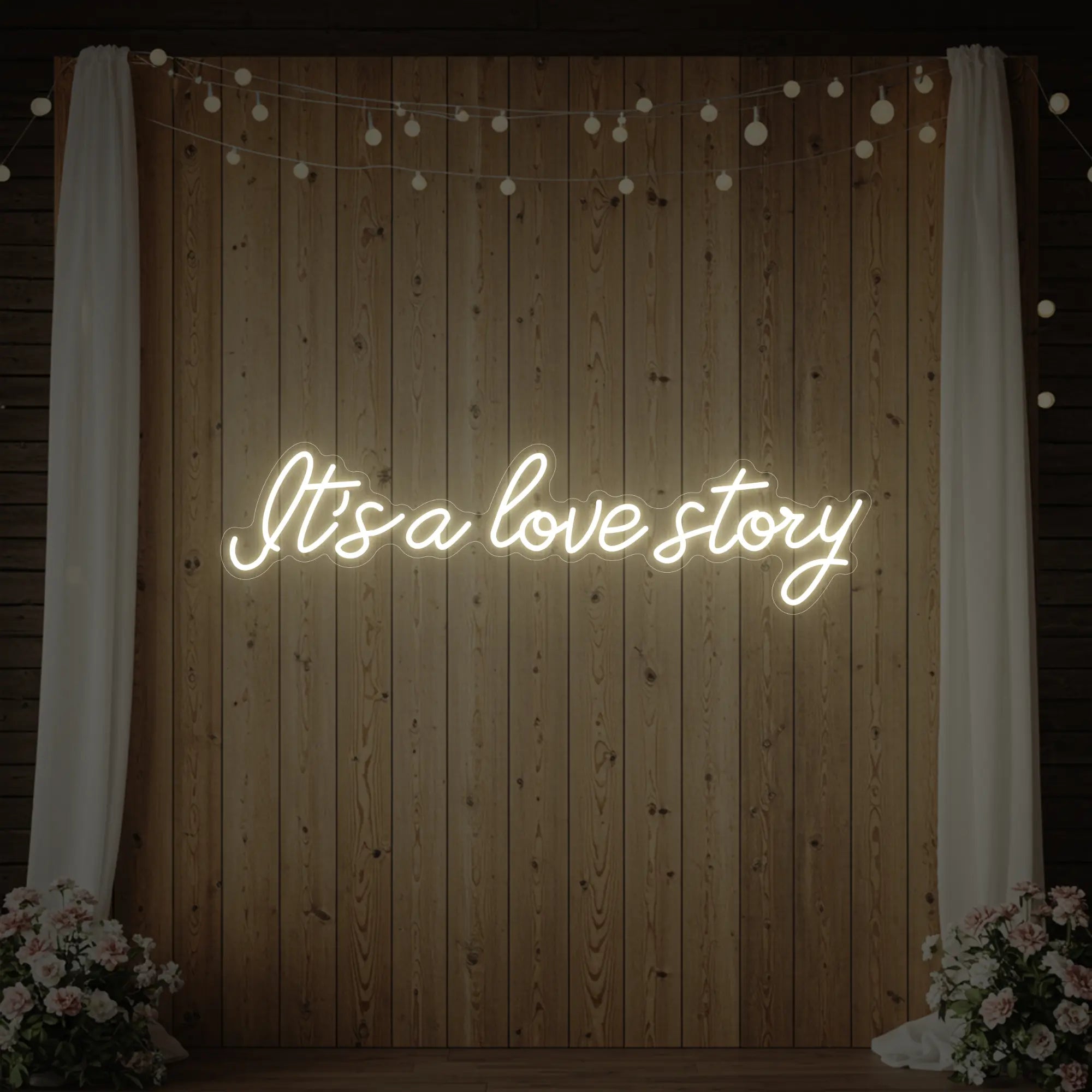 Photo of the 'It’s A Love Story' neon sign glowing in warm white against a styled interior wall.
