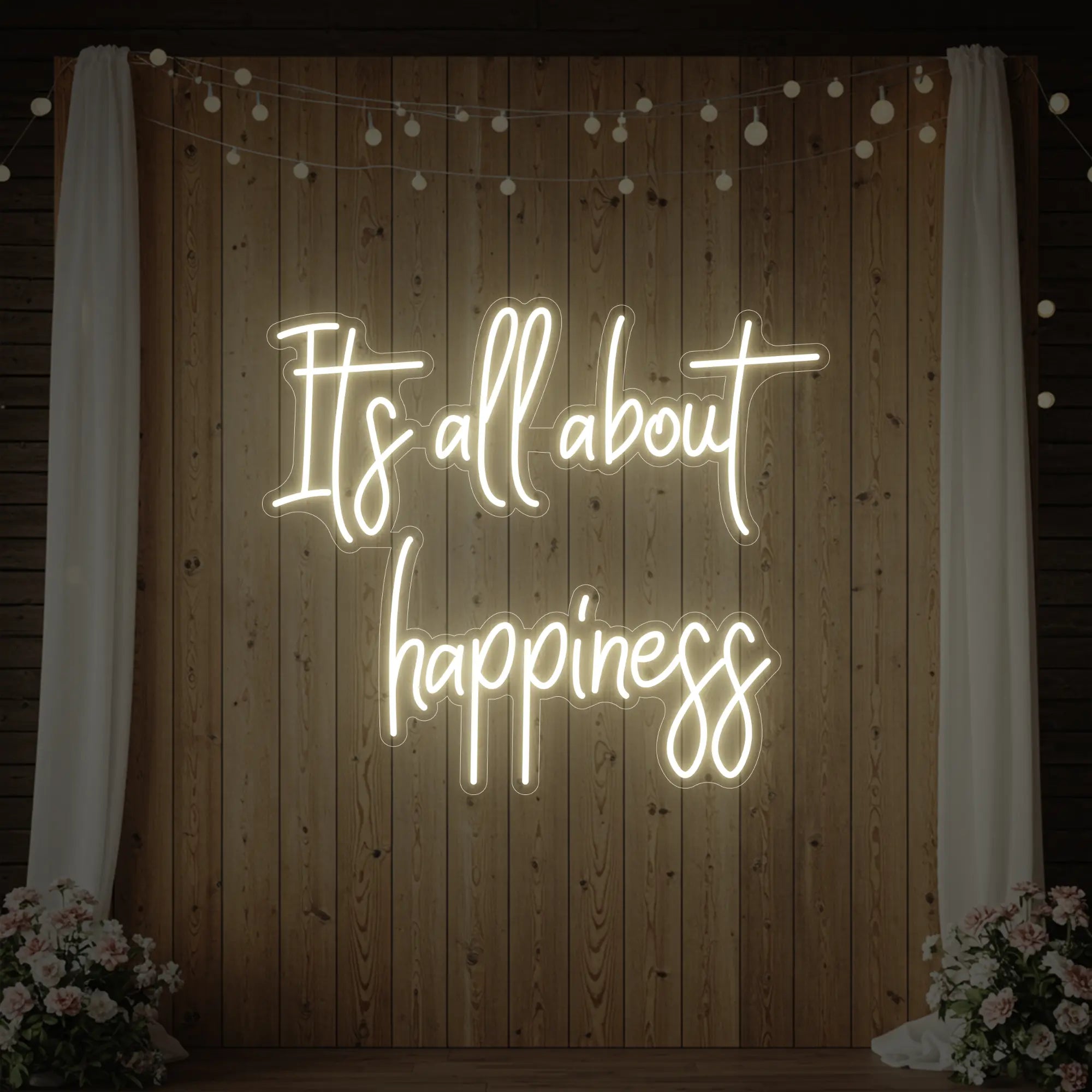 Photo of the 'It’s All About Happiness' neon sign glowing in warm white against a styled interior wall.