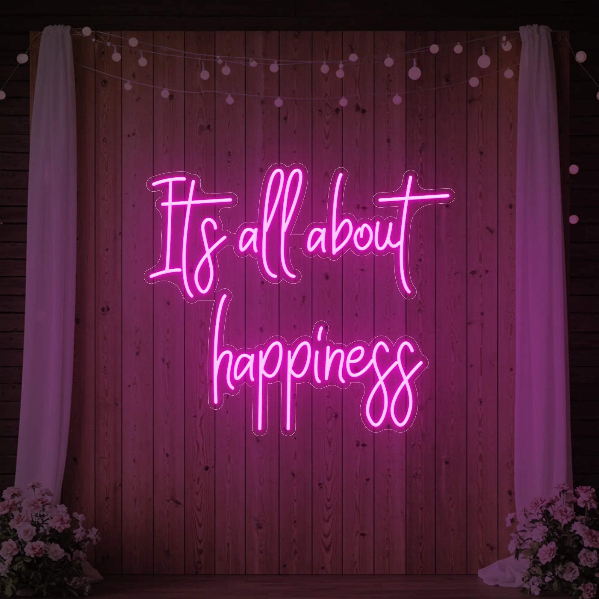 Photo of the 'It’s All About Happiness' neon sign glowing in light pink against a styled interior wall.