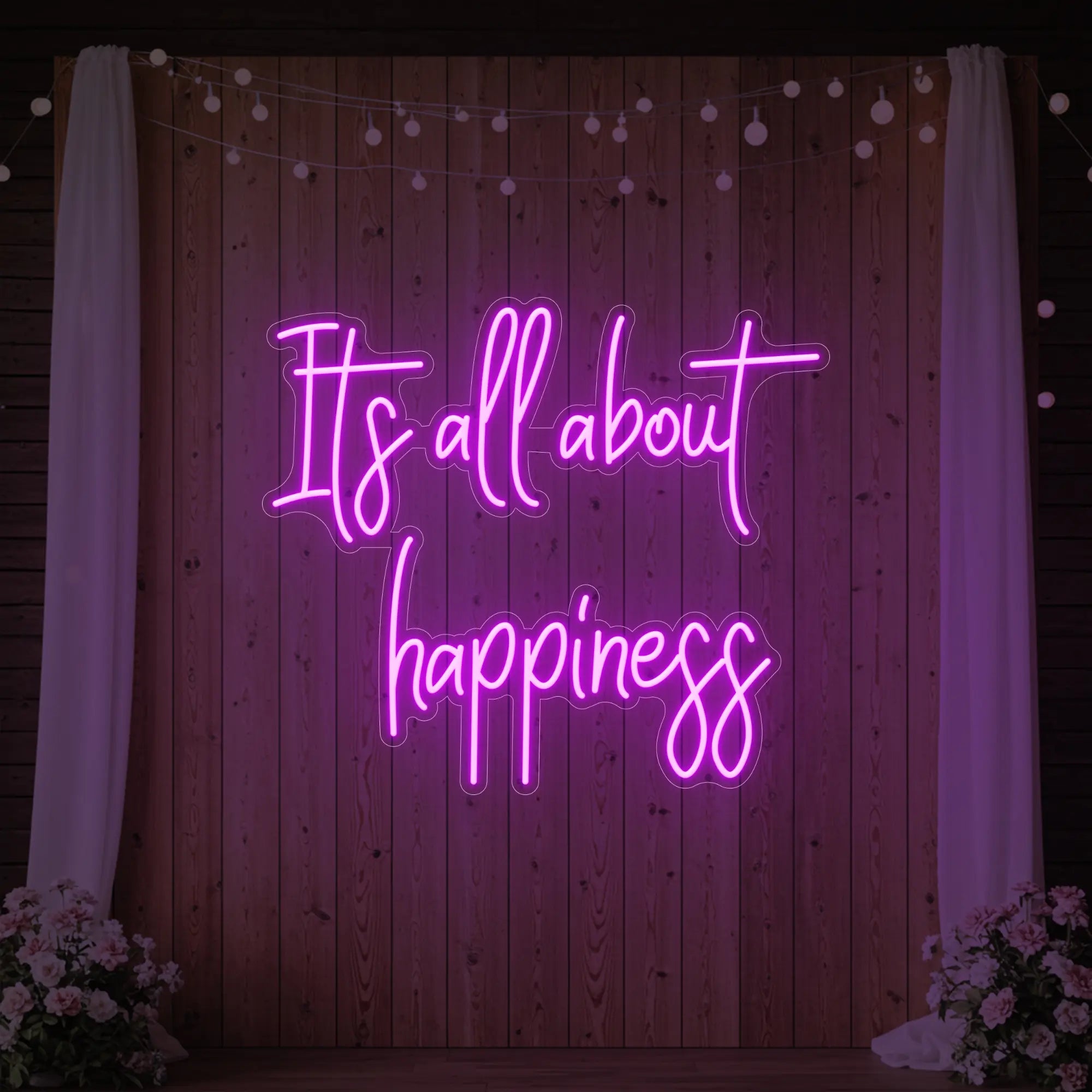 Photo of the 'It’s All About Happiness' neon sign glowing in deep pink against a styled interior wall.