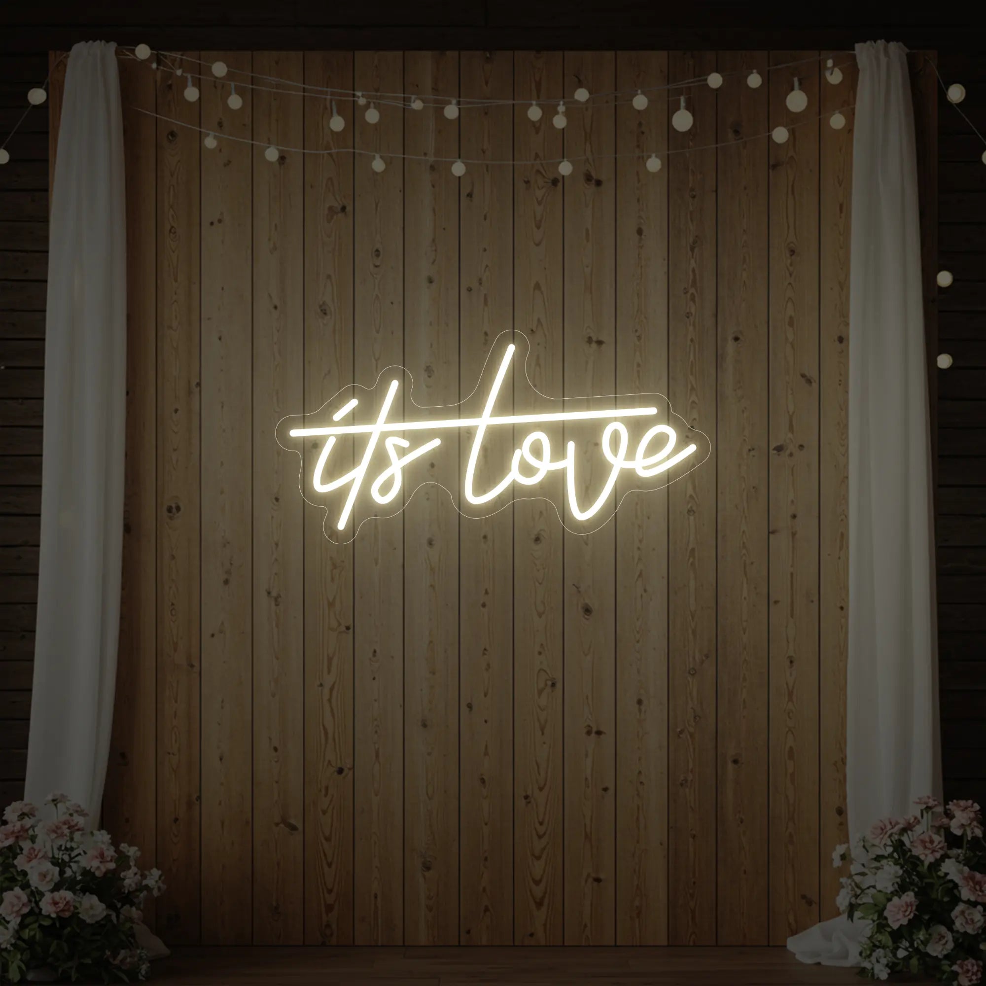 Photo of the 'It’s Love' neon sign glowing in warm white against a styled interior wall.
