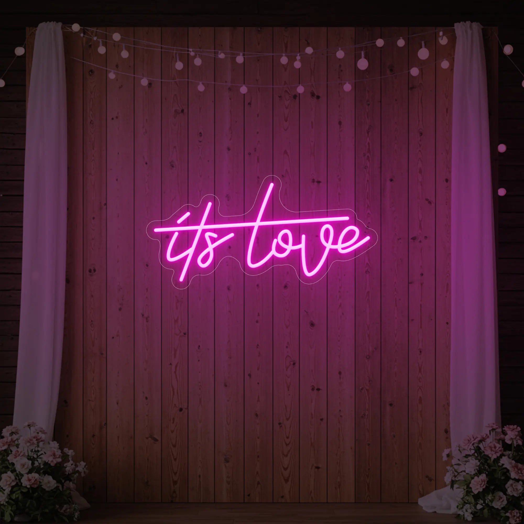 Photo of the 'It’s Love' neon sign glowing in light pink against a styled interior wall.