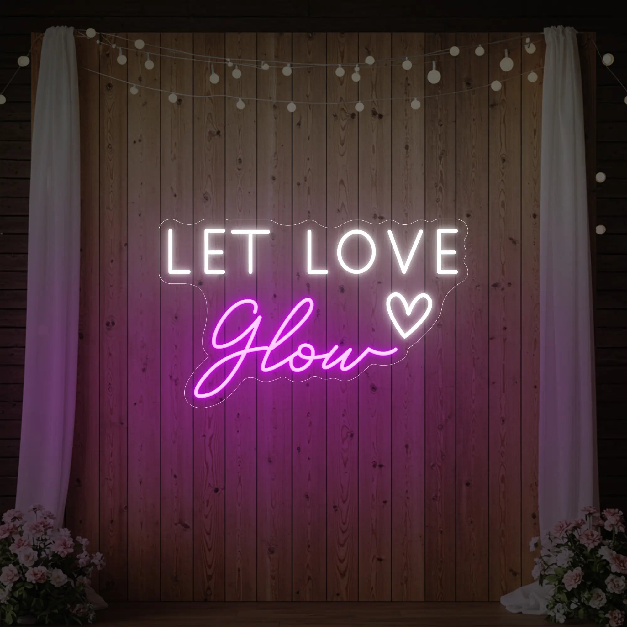 Photo of the 'Let Love Glow' neon sign glowing in deep pink against a styled interior wall.