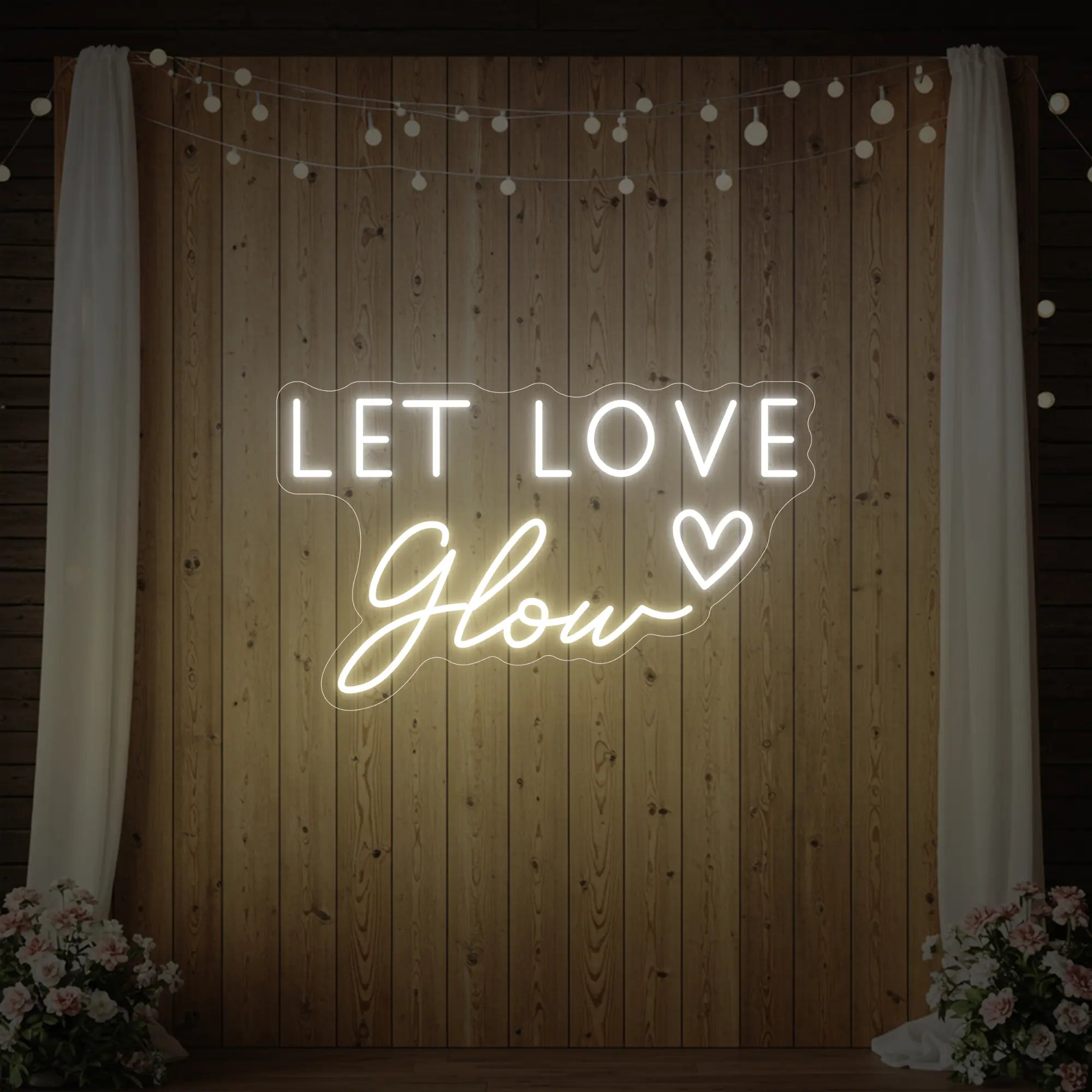 Photo of the 'Let Love Glow' neon sign glowing in warm white against a styled interior wall.