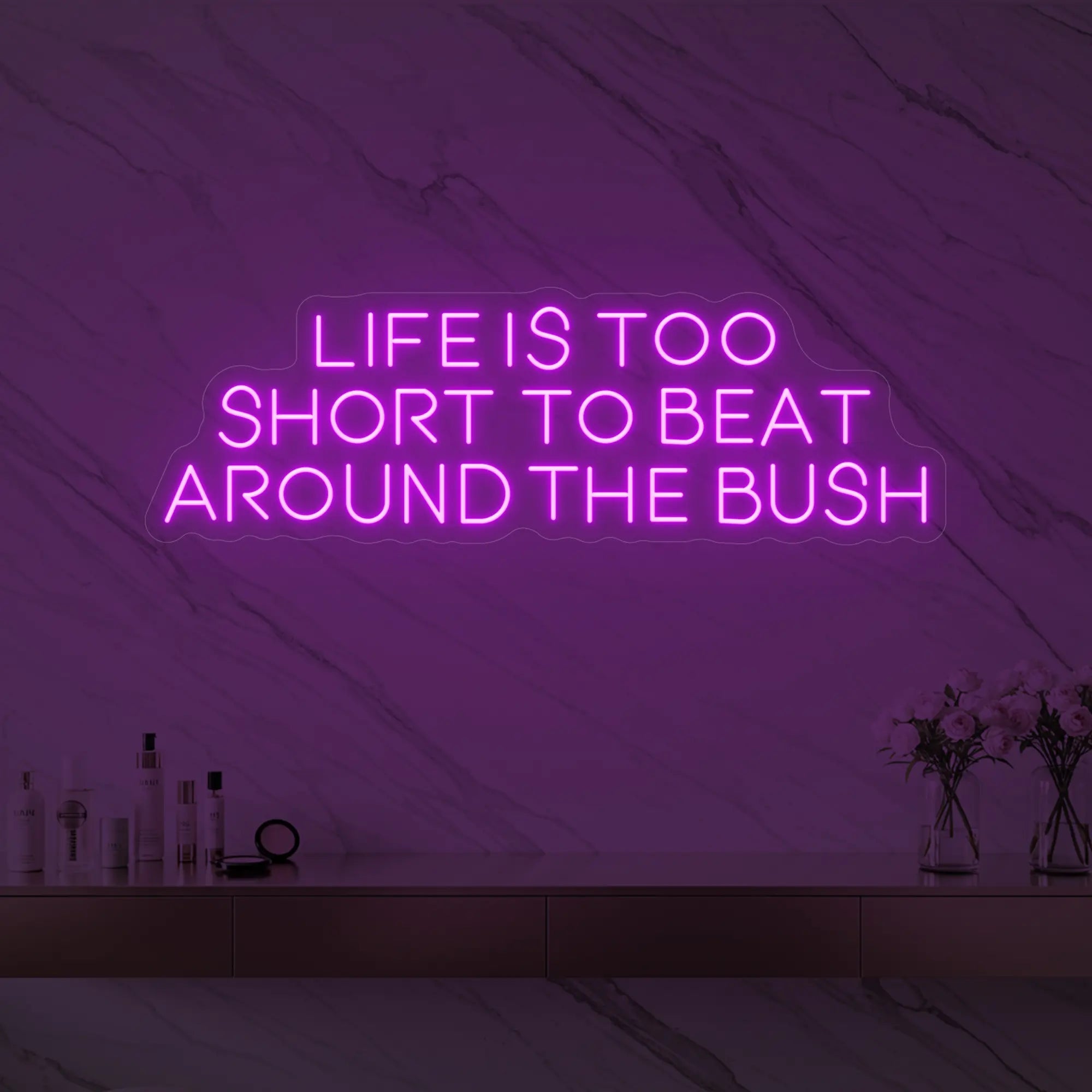 Photo of the 'Life is too short to beat around the bush' neon sign glowing in deep pink against a marble wall.