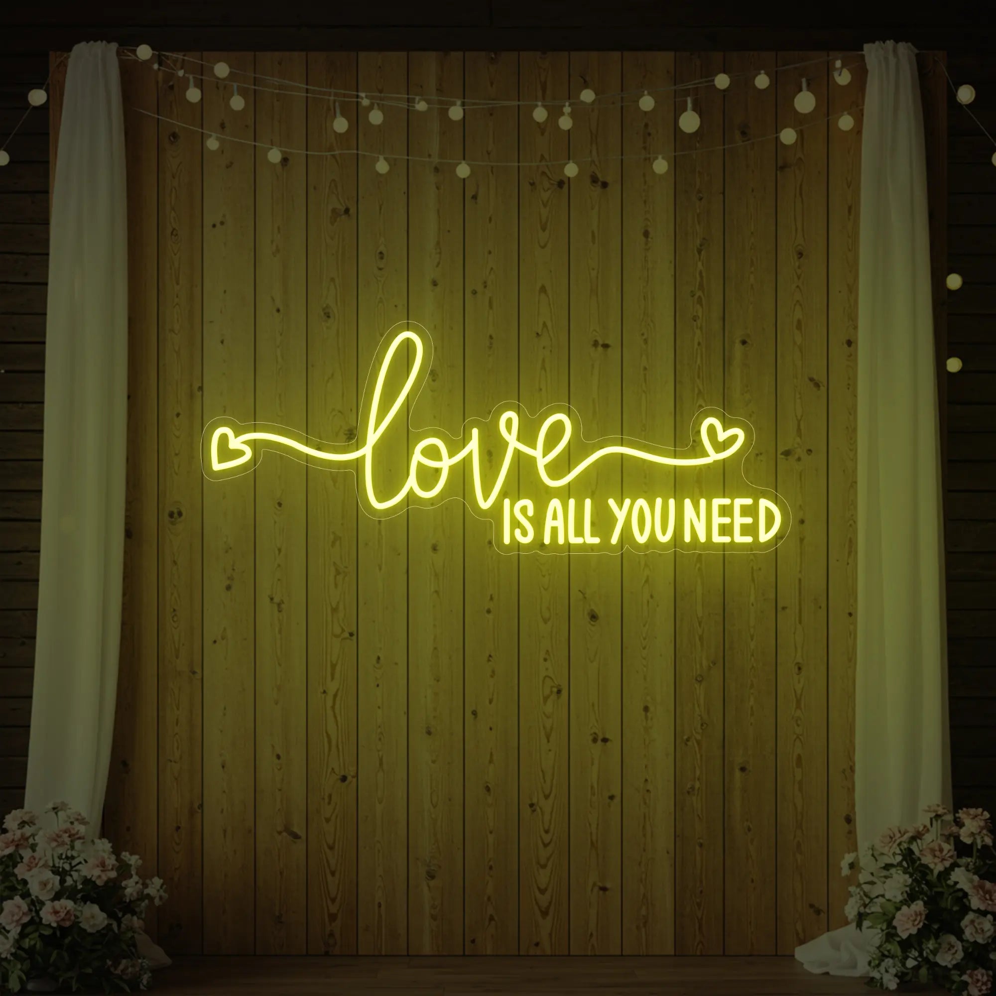 Photo of the 'Love Is All You Need' neon sign glowing in lemon yellow against a styled interior wall.