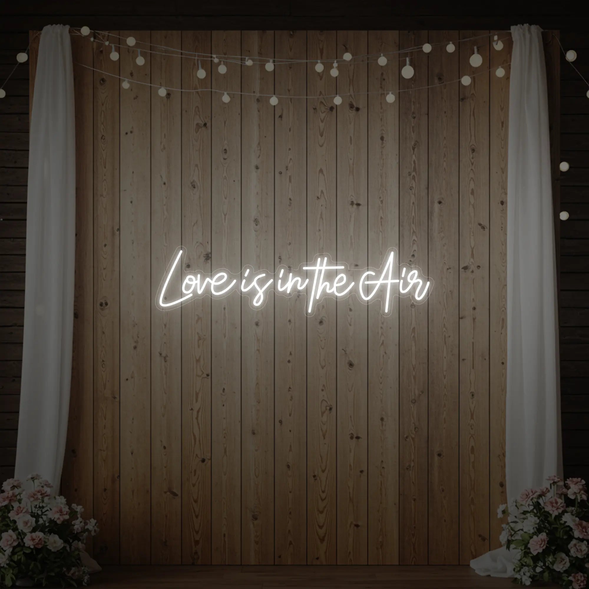 Photo of the 'Love Is In The Air' neon sign glowing in cool white against a styled interior wall.
