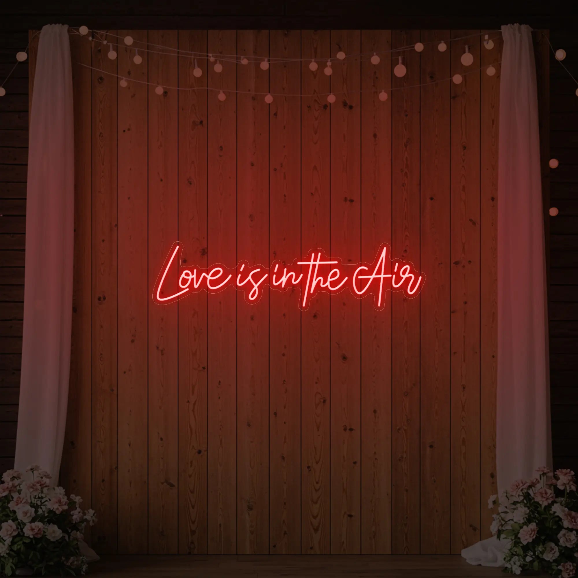 Photo of the 'Love Is In The Air' neon sign glowing in red against a styled interior wall.