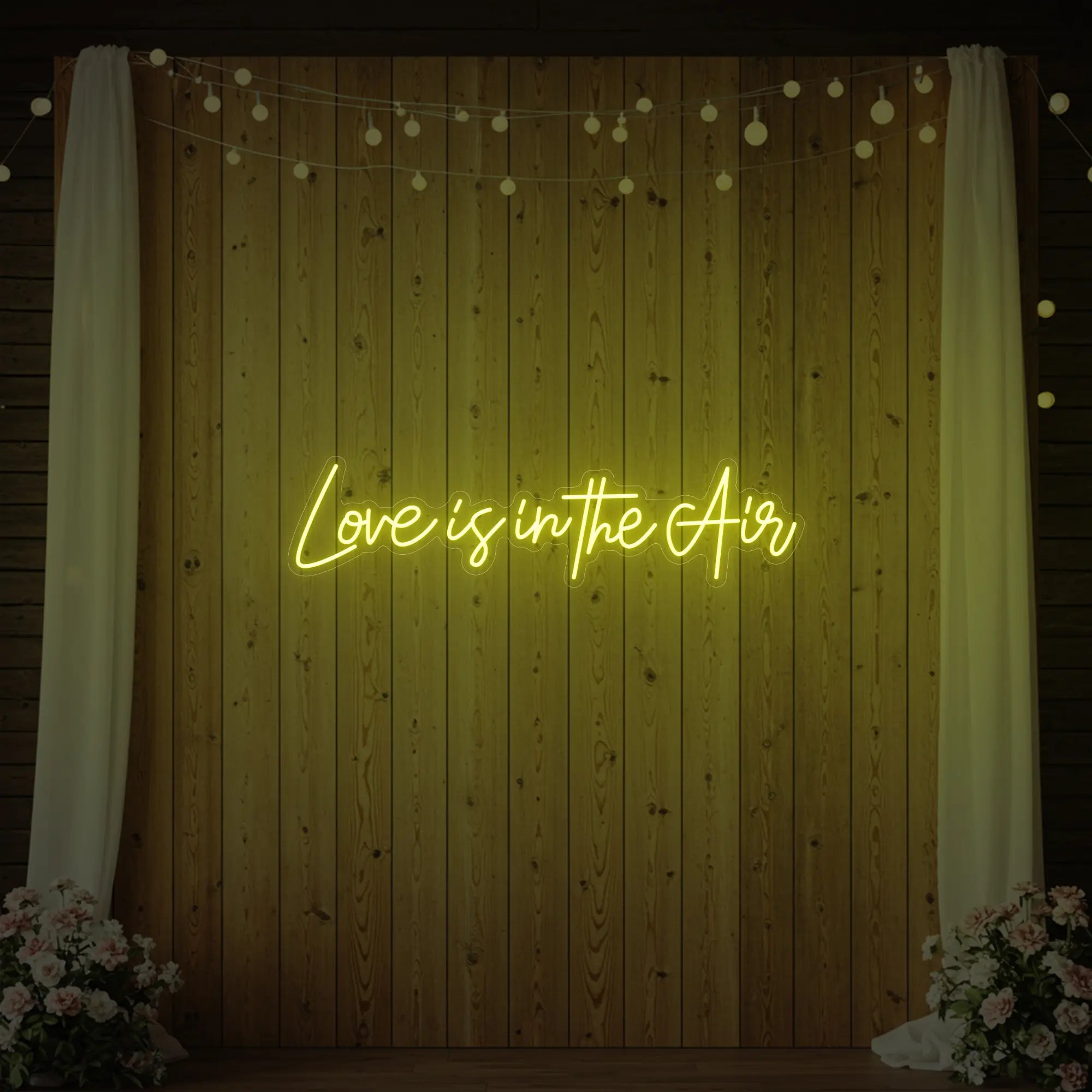 Photo of the 'Love Is In The Air' neon sign glowing in lemon yellow against a styled interior wall.
