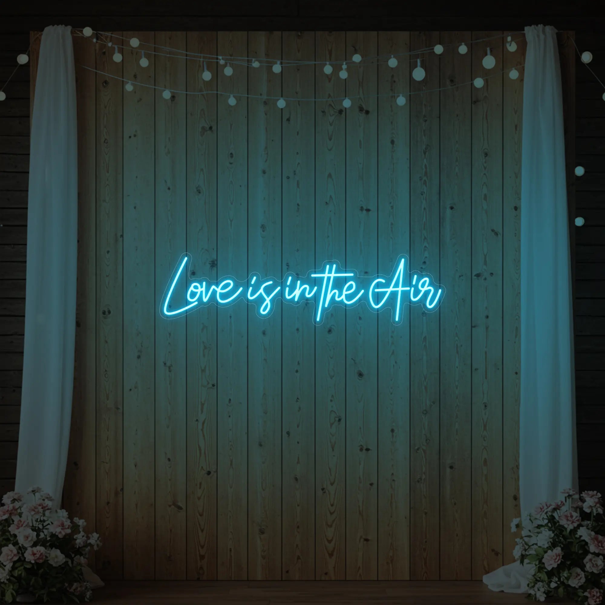 Photo of the 'Love Is In The Air' neon sign glowing in ice blue against a styled interior wall.