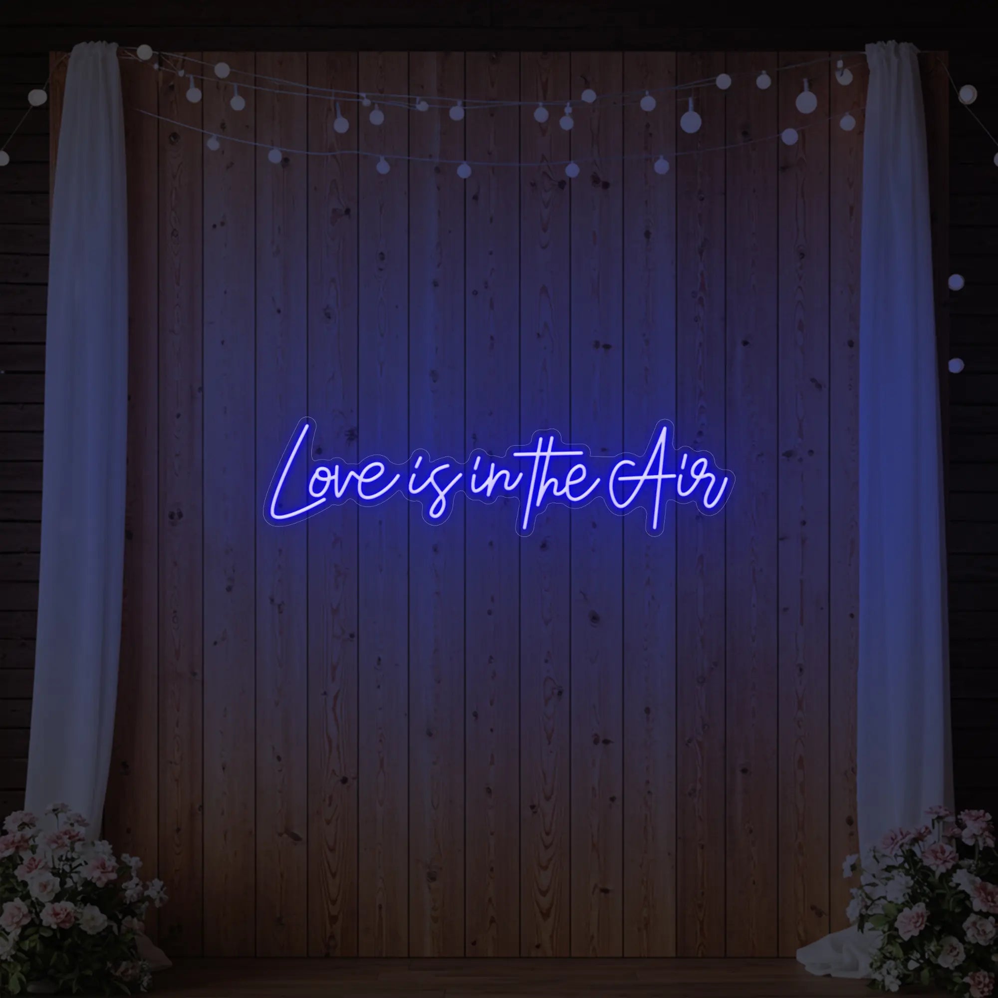 Photo of the 'Love Is In The Air' neon sign glowing in deep blue against a styled interior wall.