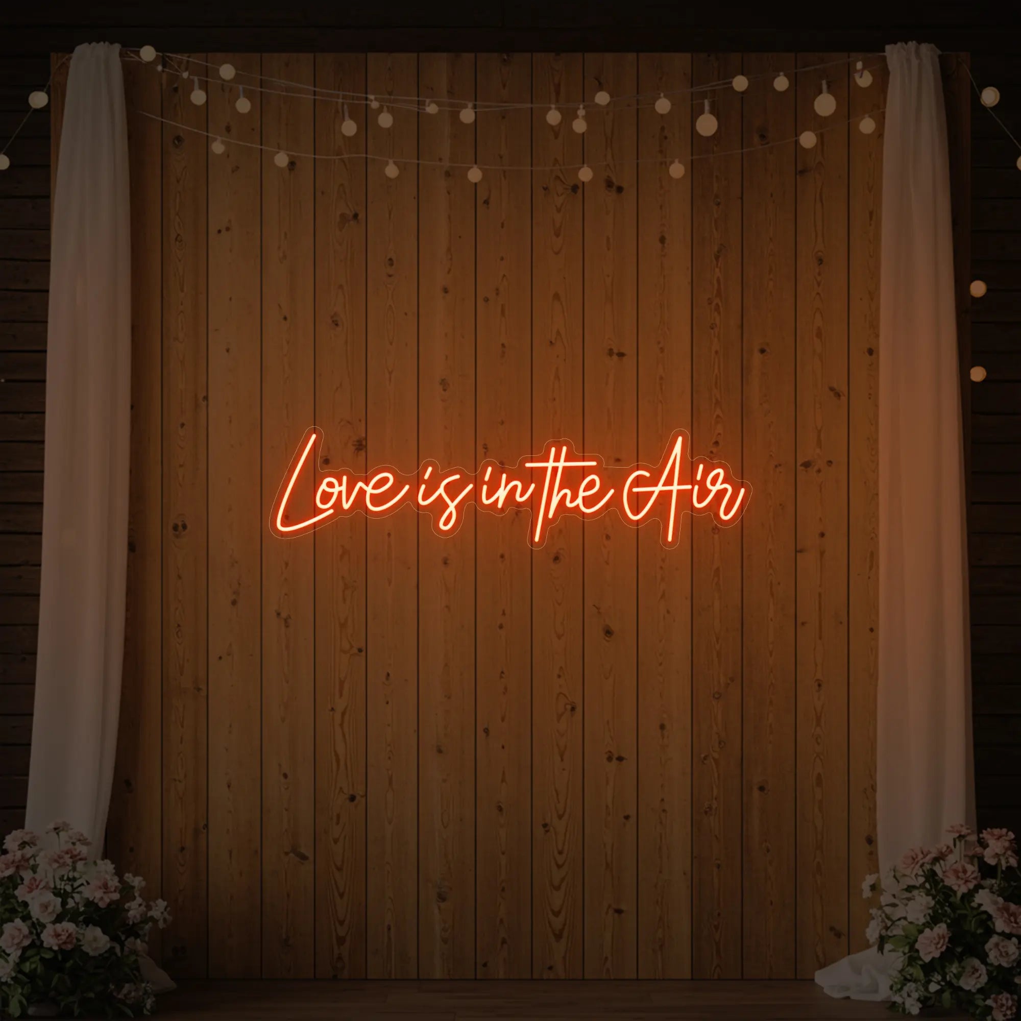 Photo of the 'Love Is In The Air' neon sign glowing in golden yellow against a styled interior wall.