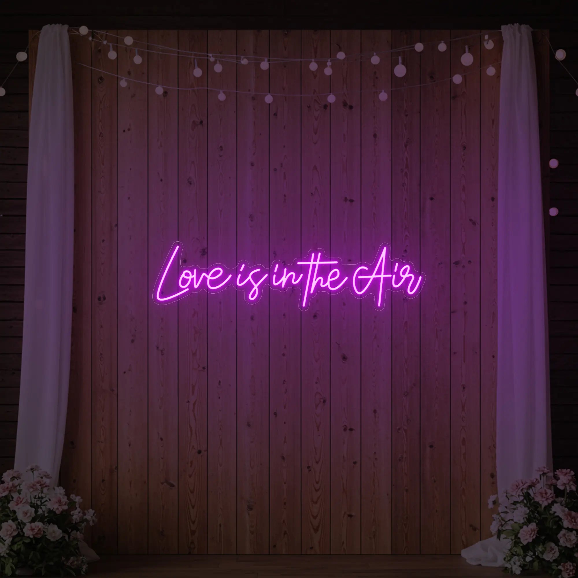 Photo of the 'Love Is In The Air' neon sign glowing in deep pink against a styled interior wall.