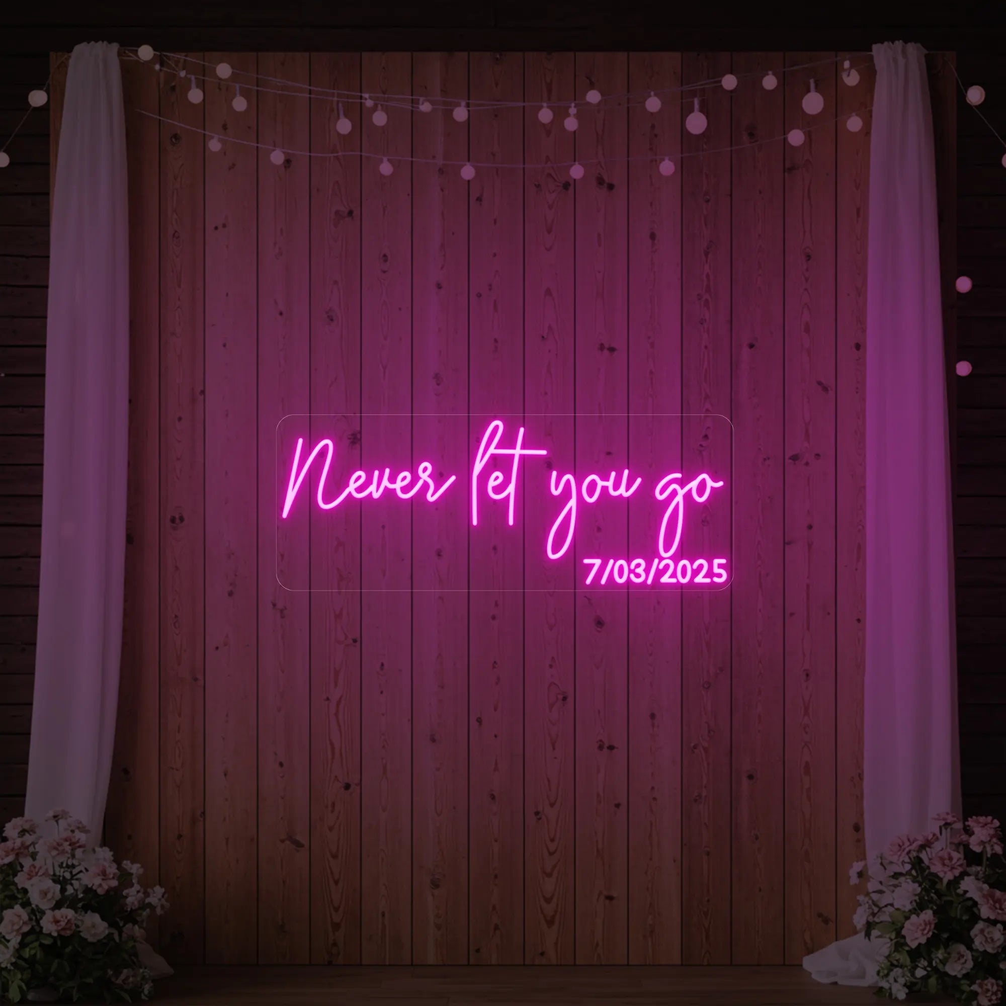'Never Let You Go' neon sign glowing in deep pink against a styled interior wall.
