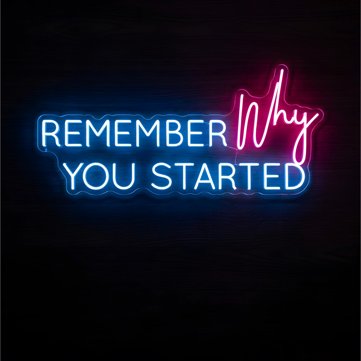 Remember Why You Started LED Neon Sign with blue uppercase lettering and pink script on clear acrylic against a dark wood background, suited to home offices and creative workspaces.