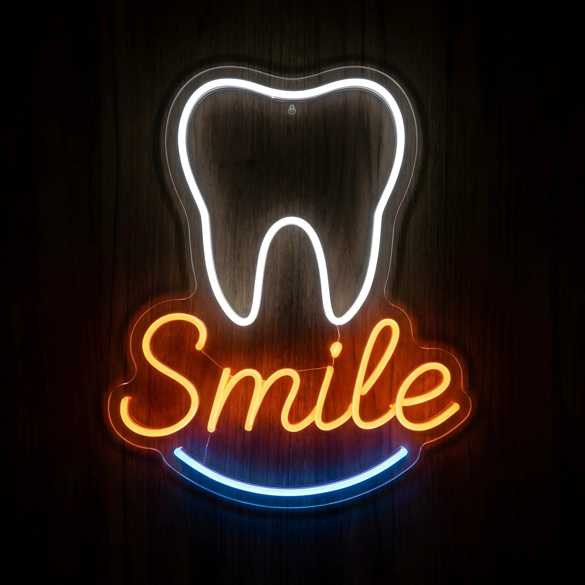 Tooth Smile Script LED neon sign featuring a glowing white tooth outline, orange cursive Smile lettering, and blue curved smile accent on clear acrylic backing against a dark wooden wall.