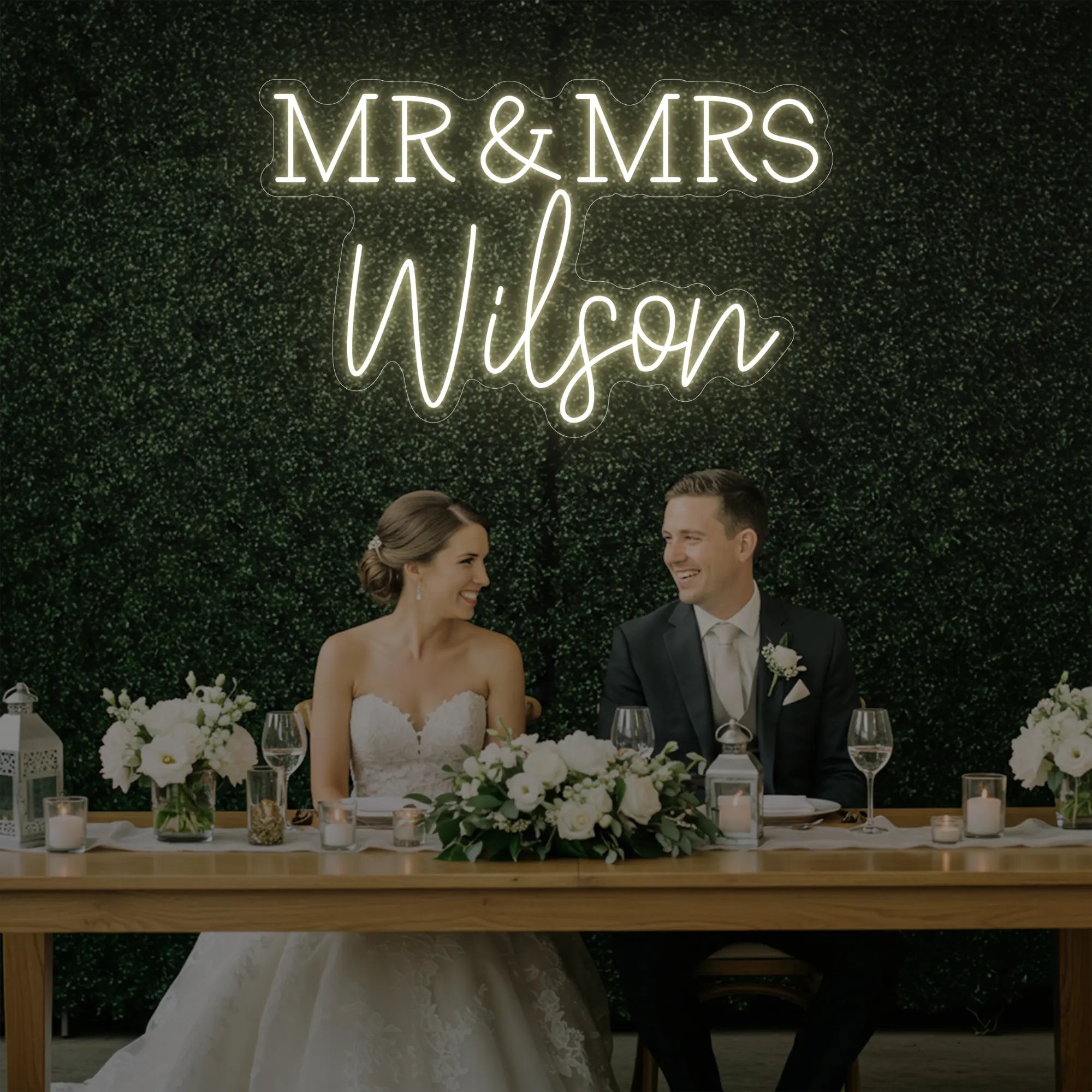 Photo of the 'Wedding Last Names Custom Neon Sign V2' neon sign glowing in warm white against a styled interior wall.