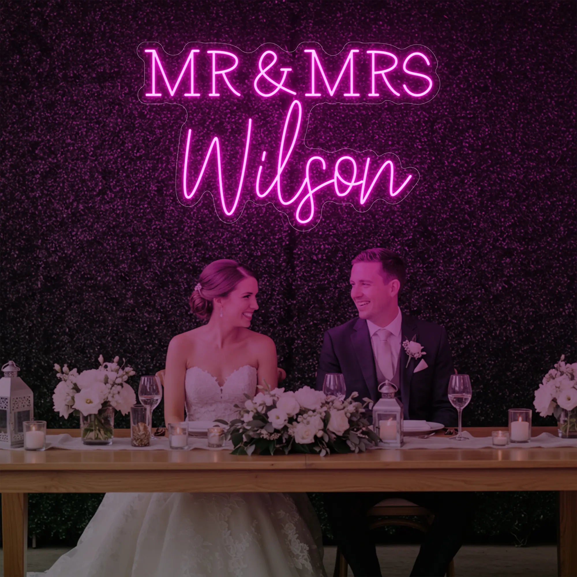 Photo of the 'Wedding Last Names Custom Neon Sign V2' neon sign glowing in light pink against a styled interior wall.