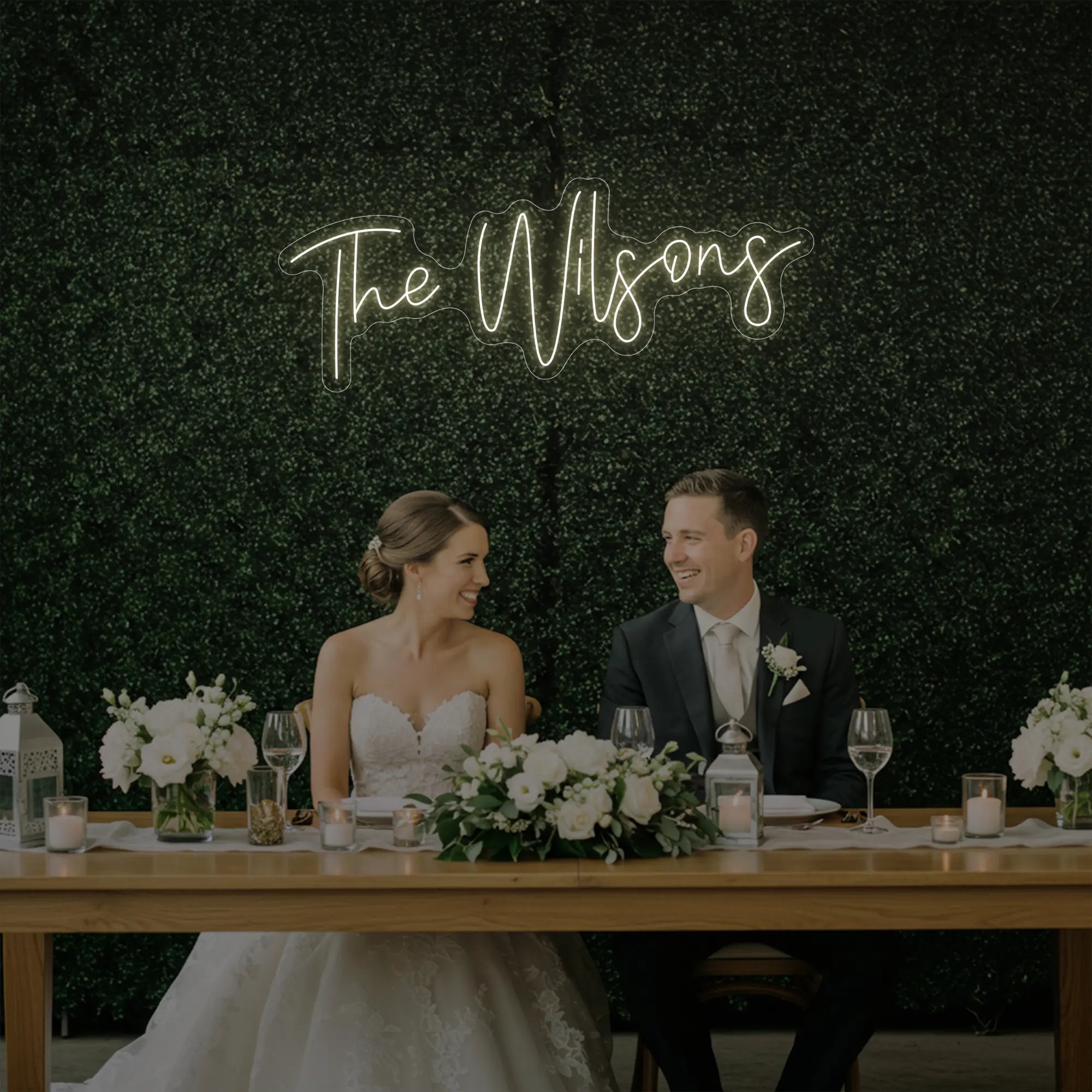 Photo of the 'Wedding Last Names Custom Neon Sign V4' neon sign glowing in warm white against a styled interior wall.