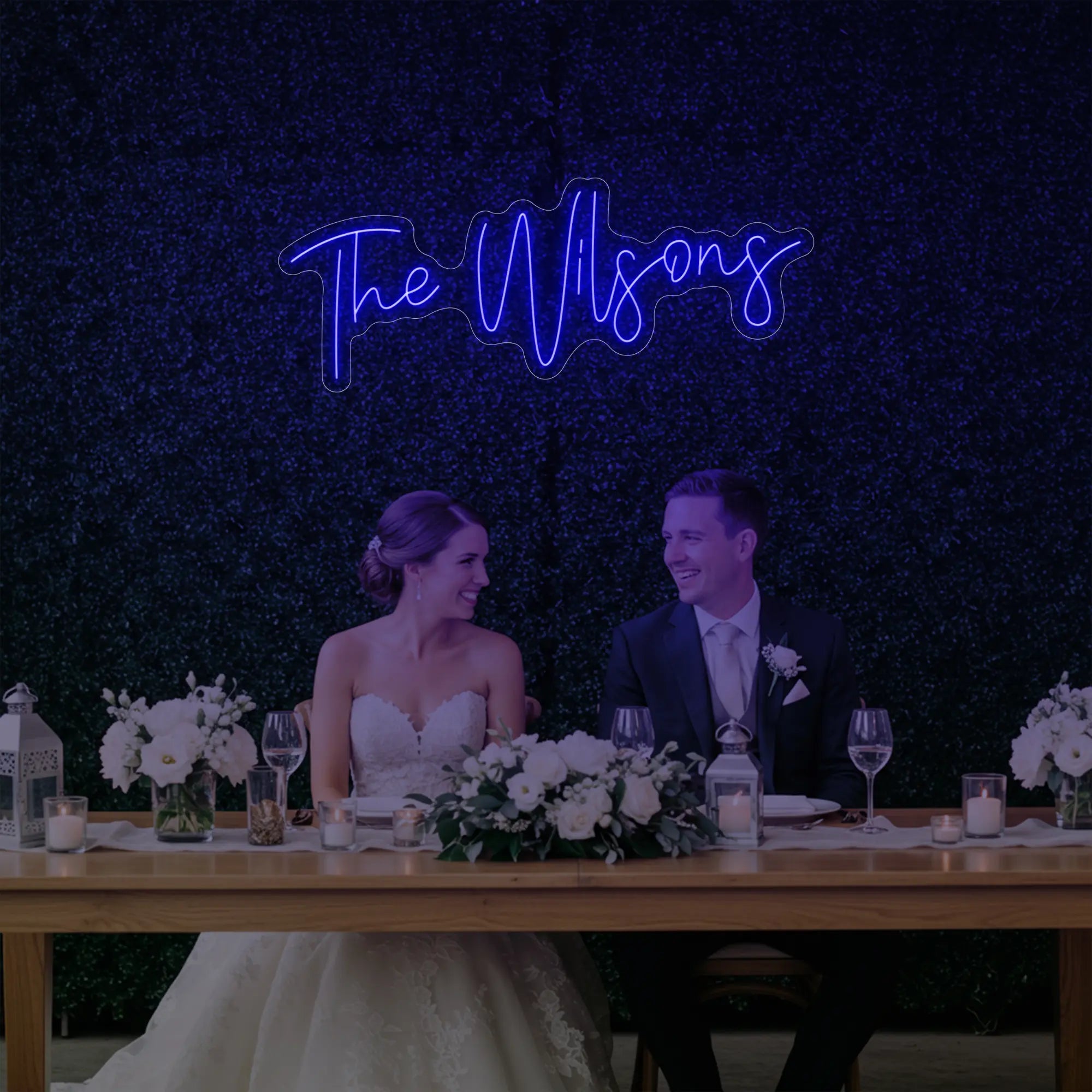 Photo of the 'Wedding Last Names Custom Neon Sign V4' neon sign glowing in deep blue against a styled interior wall.