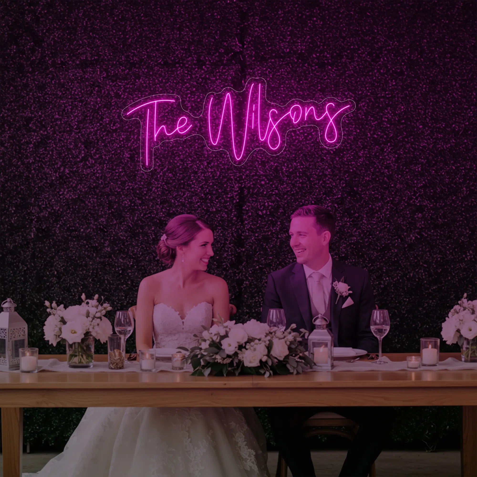 Photo of the 'Wedding Last Names Custom Neon Sign V4' neon sign glowing in light pink against a styled interior wall.