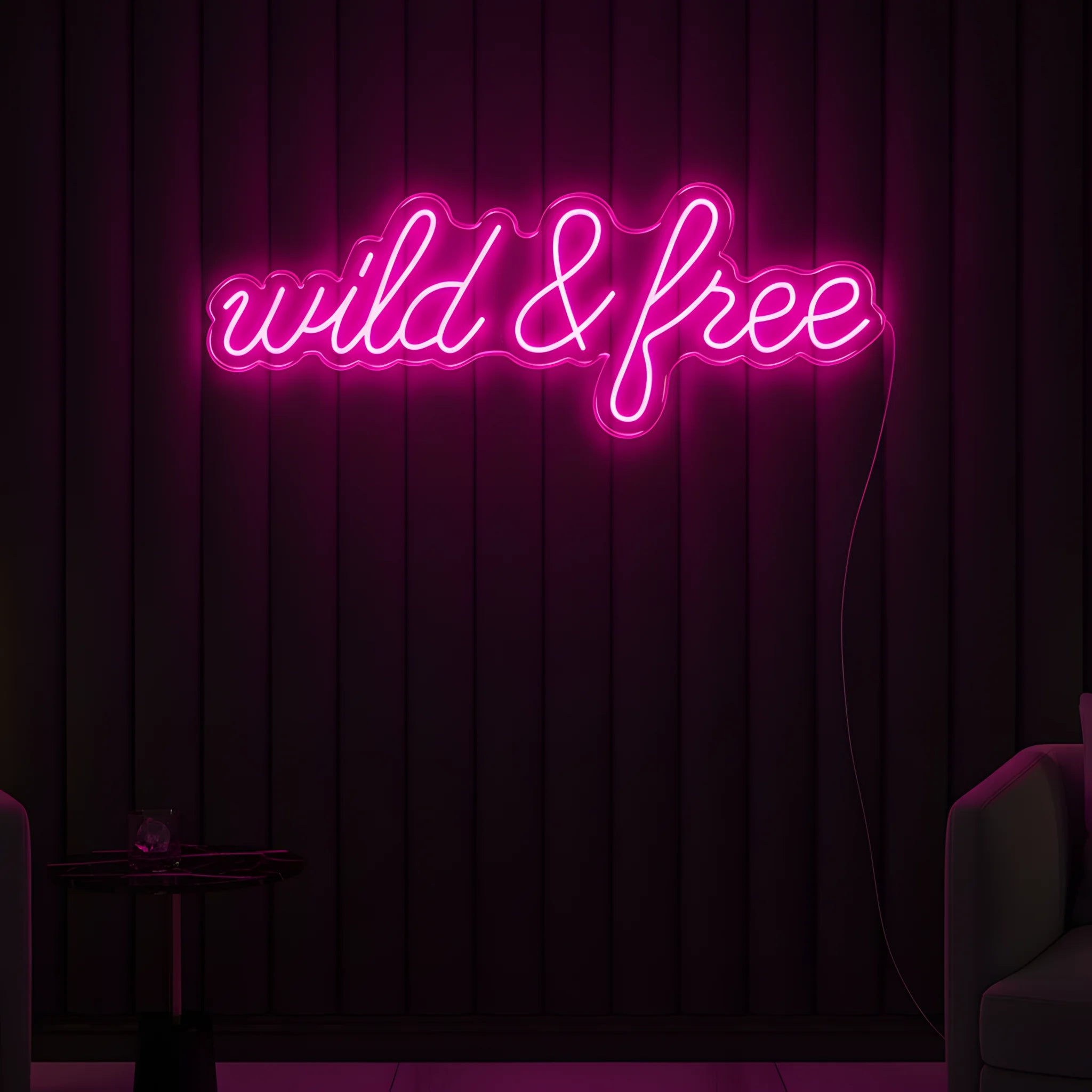 Photo of the 'Wild & Free' neon sign glowing in pink against a modern boho-inspired wall.