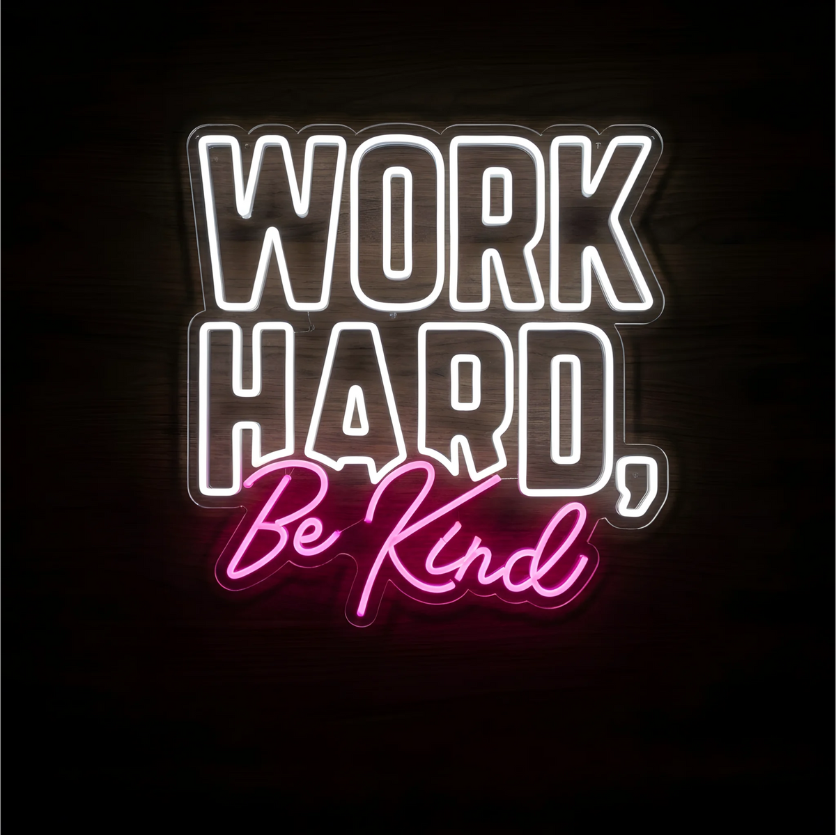 “WORK HARD, Be Kind” LED Neon Sign with white block lettering and pink script on clear acrylic backing against a dark wood background, suitable for offices, classrooms, and shared workspaces.