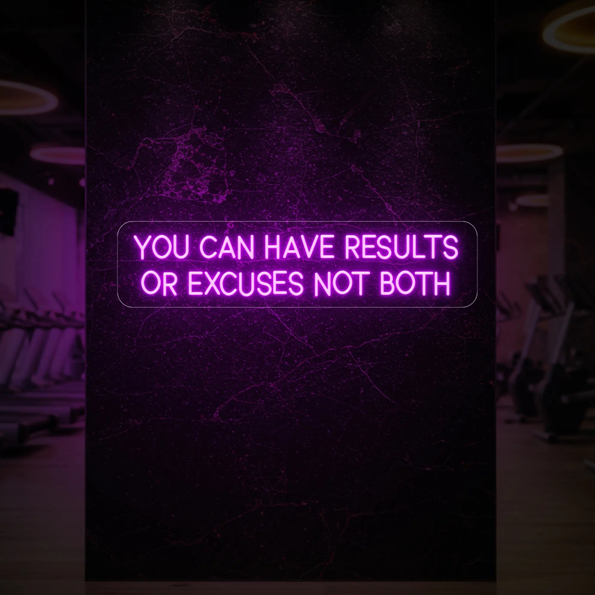 'YOU CAN HAVE RESULTS OR EXCUSES NOT BOTH' neon sign glowing in deep pink against a styled interior wall.