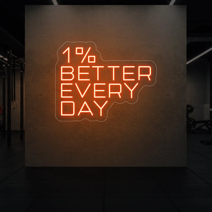 '1% Better Every Day' neon sign glowing in golden yellow against a styled interior wall.