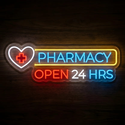 24 Hour Pharmacy Open LED Neon Sign featuring a white heart with red medical cross, blue PHARMACY lettering, and multicolor OPEN 24 HRS text on a dark wooden wall.