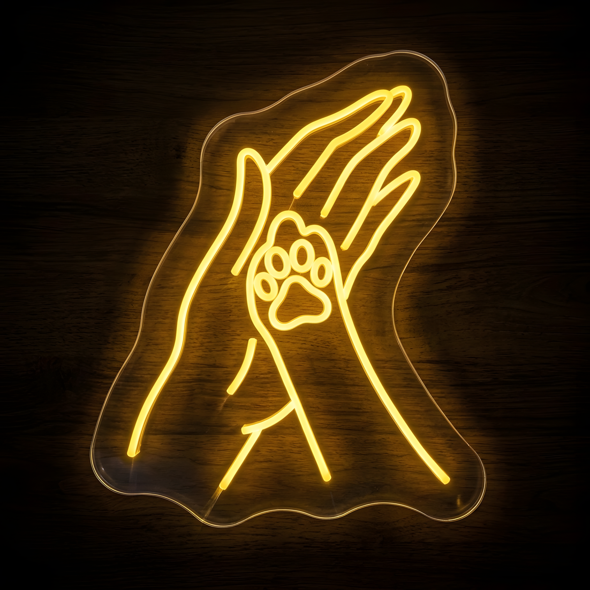 Helping Paw LED Neon Sign featuring warm yellow line art of a human hand gently touching a pet paw, mounted on clear acrylic against a dark wood wall for veterinary clinics, animal shelters, pet care businesses, and animal lover decor.