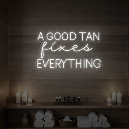 Photo of the 'A GOOD TAN fixes EVERYTHING' neon sign glowing in cool white against a styled interior wall.