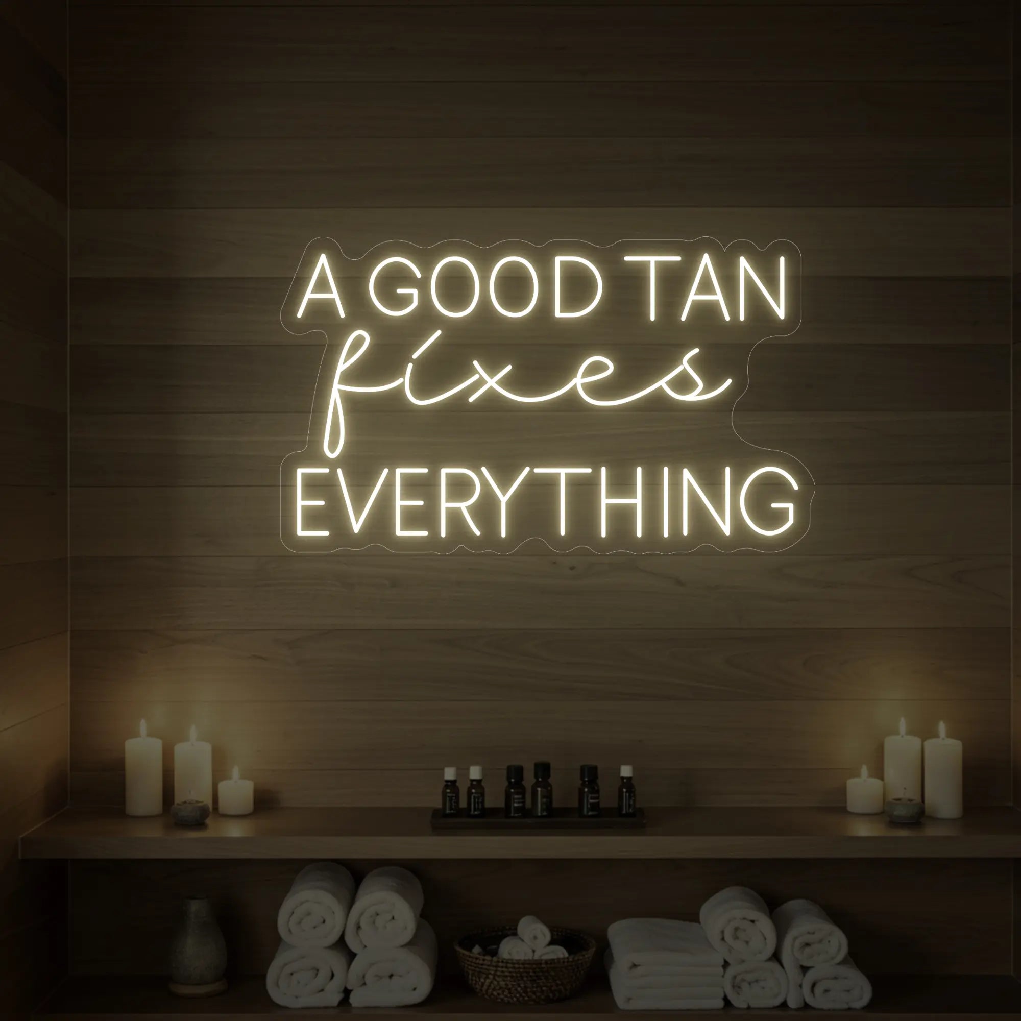 Photo of the 'A GOOD TAN fixes EVERYTHING' neon sign glowing in warm white against a styled interior wall.