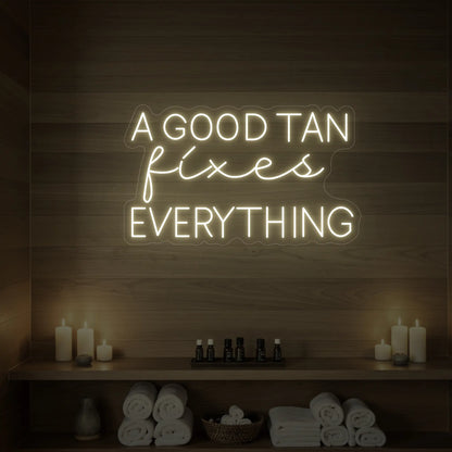 Photo of the 'A GOOD TAN fixes EVERYTHING' neon sign glowing in warm white against a styled interior wall.