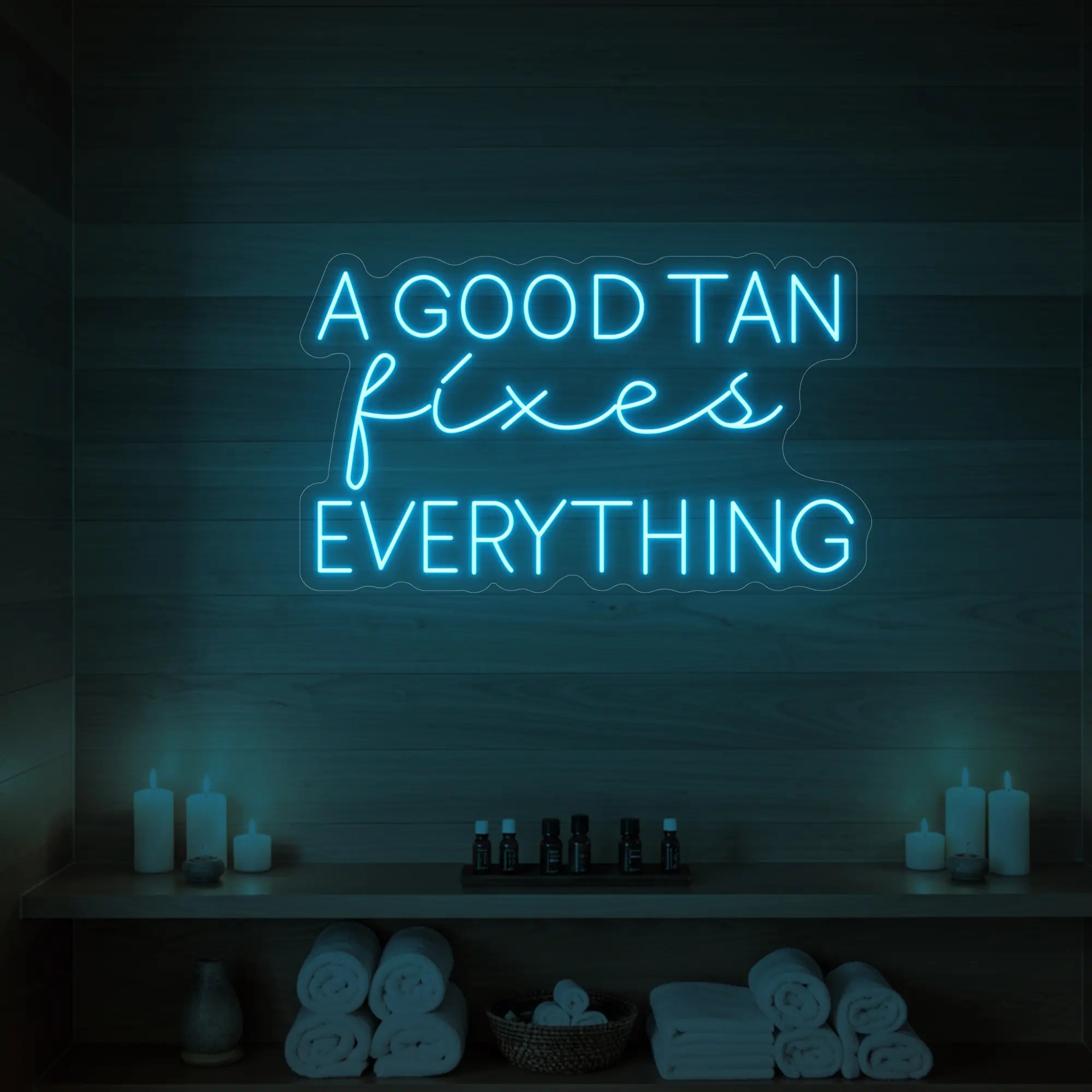 Photo of the 'A GOOD TAN fixes EVERYTHING' neon sign glowing in ice blue against a styled interior wall.